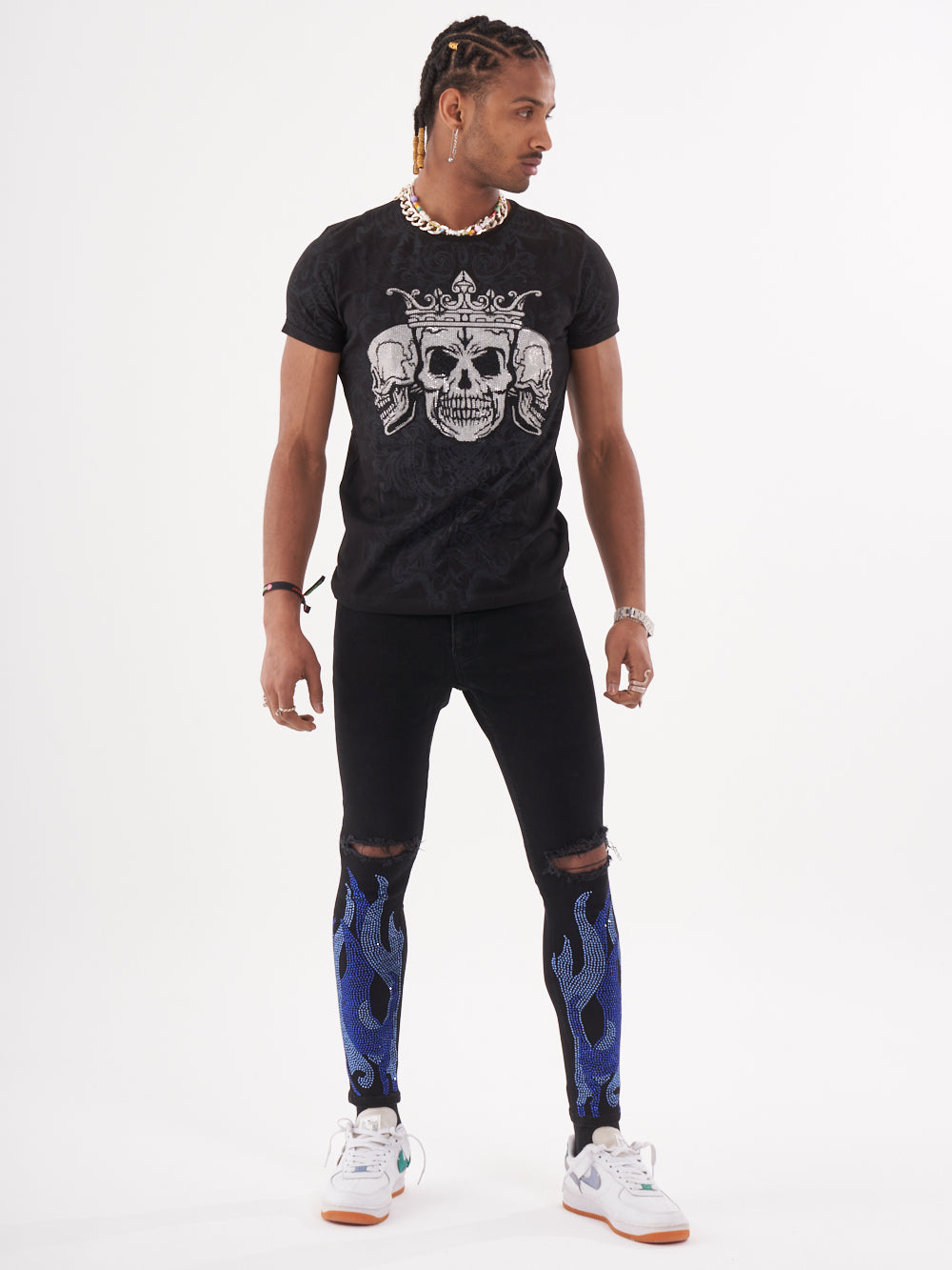 A man wearing a TRINITY T-Shirt in black with a skeleton print and blue jeans.