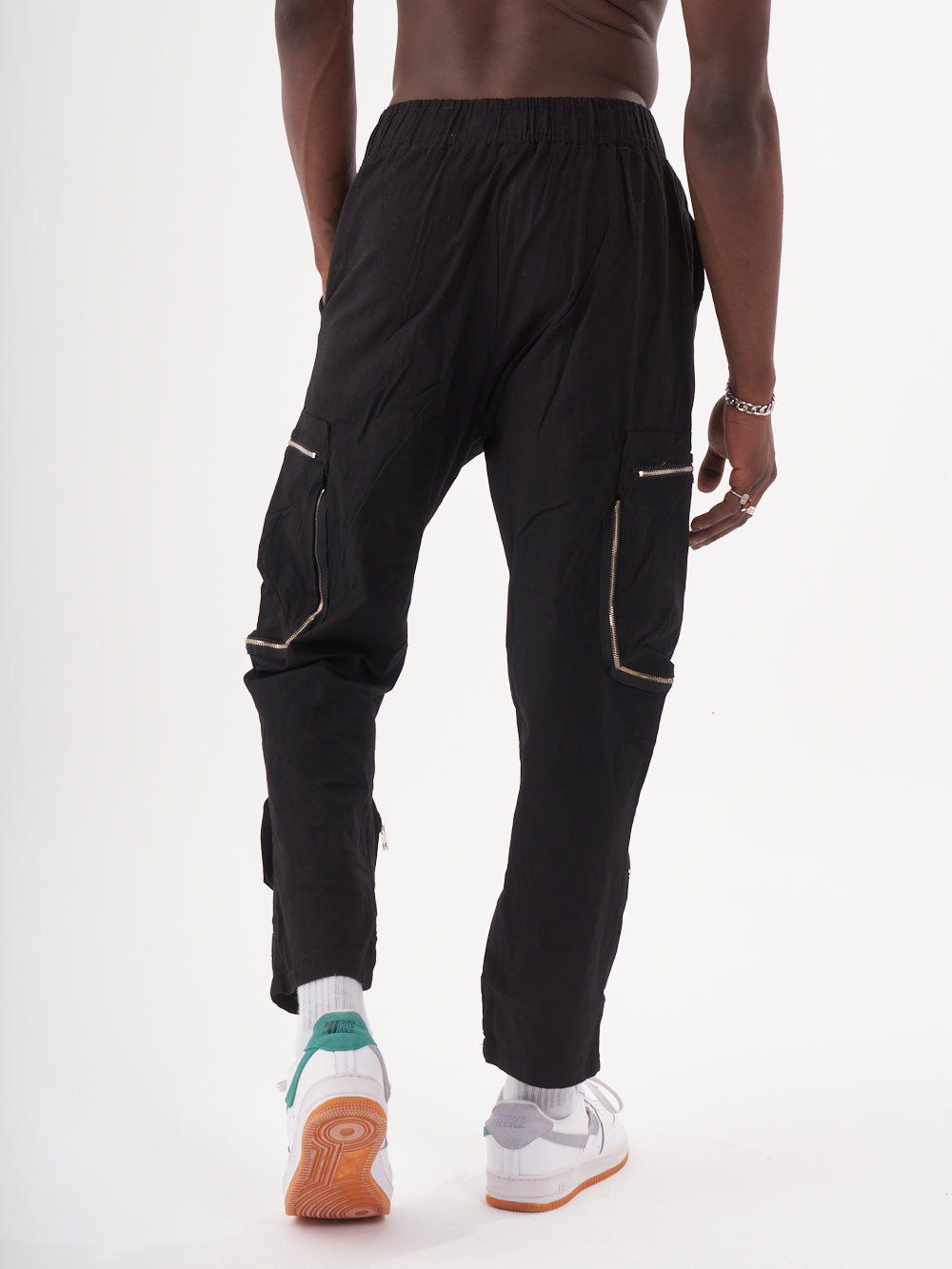 Person wearing MULTI-ZIPPER POCKET JOGGER // BLACK with an elastic drawstring waist and white sneakers, standing against a plain white background.