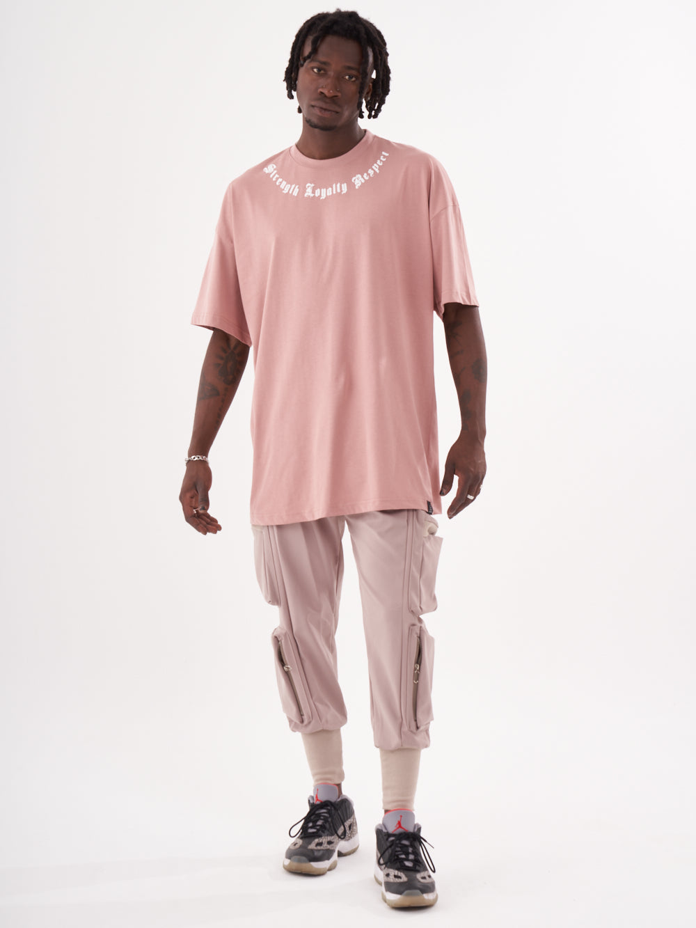 A man wearing a pink CREED T-SHIRT and cargo pants.