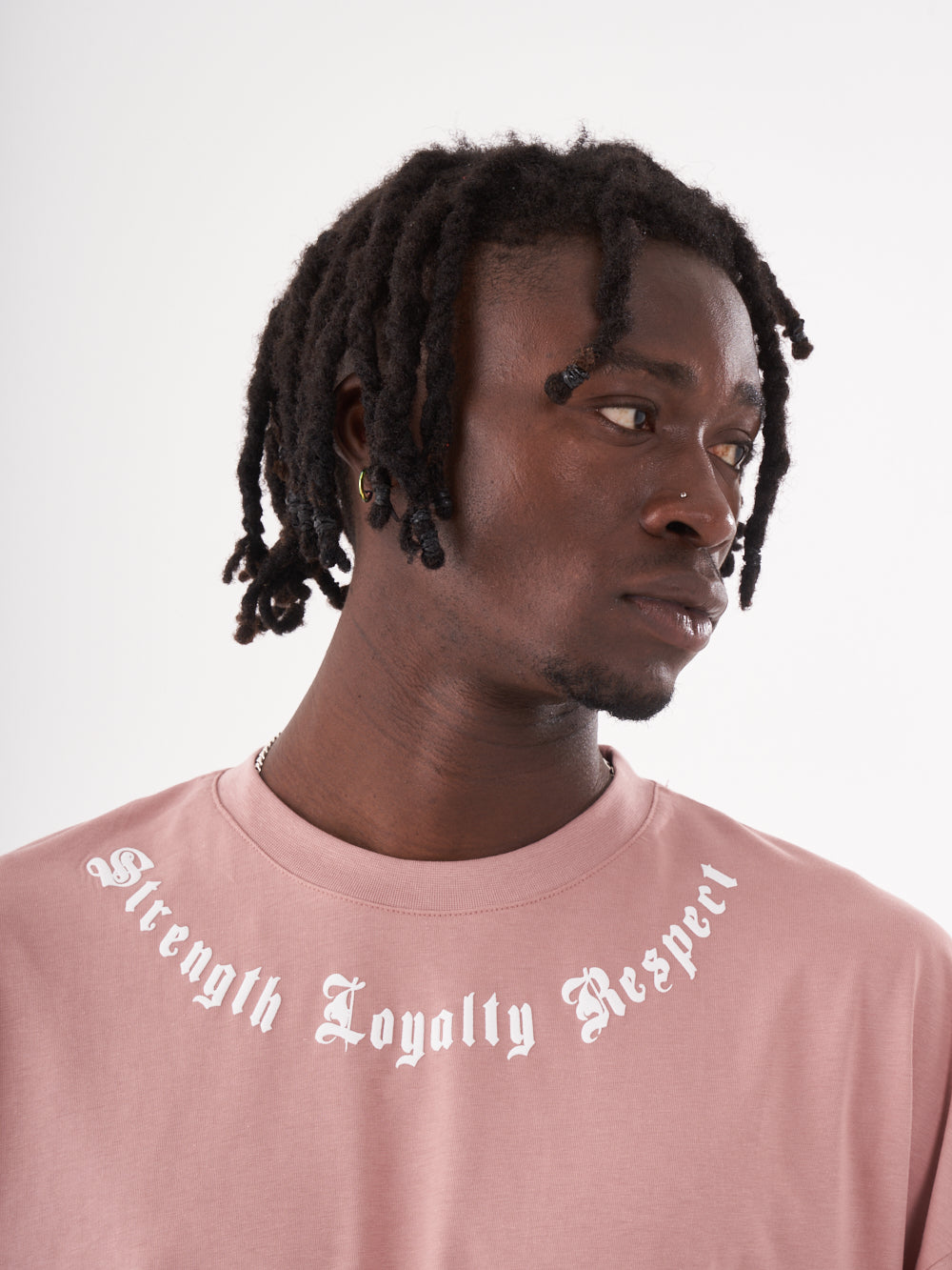 A man with dreadlocks wearing a pink CREED T-SHIRT that says strength loyalty respect.