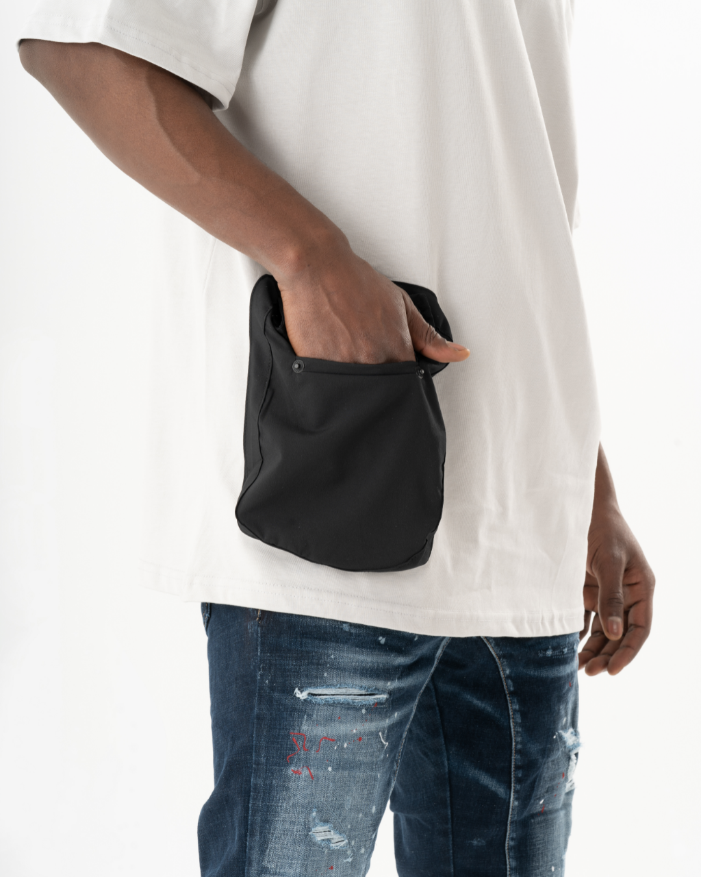 A man wearing an ELEVATE T-SHIRT and jeans holding a black pocket pouch.