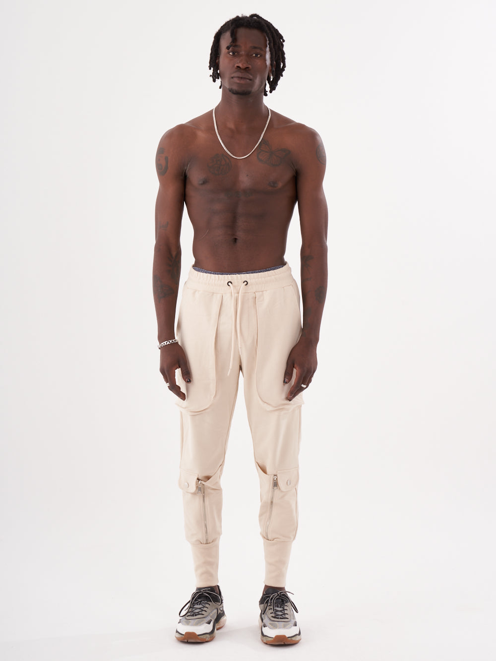 A stylish man with no shirt and no pants is standing in front of a white background wearing comfortable GUERRILLA | BEIGE joggers.