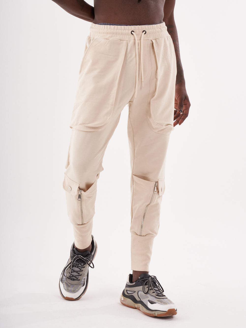 A man wearing GUERRILLA | BEIGE sweatpants and sneakers.