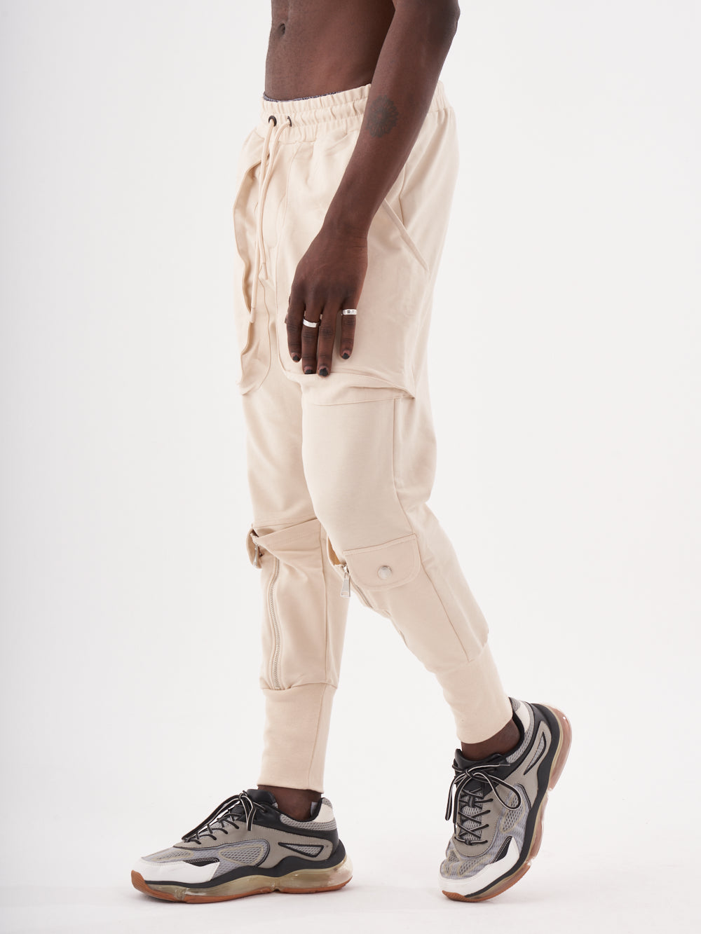 A man wearing GUERRILLA | BEIGE sweatpants and sneakers.
