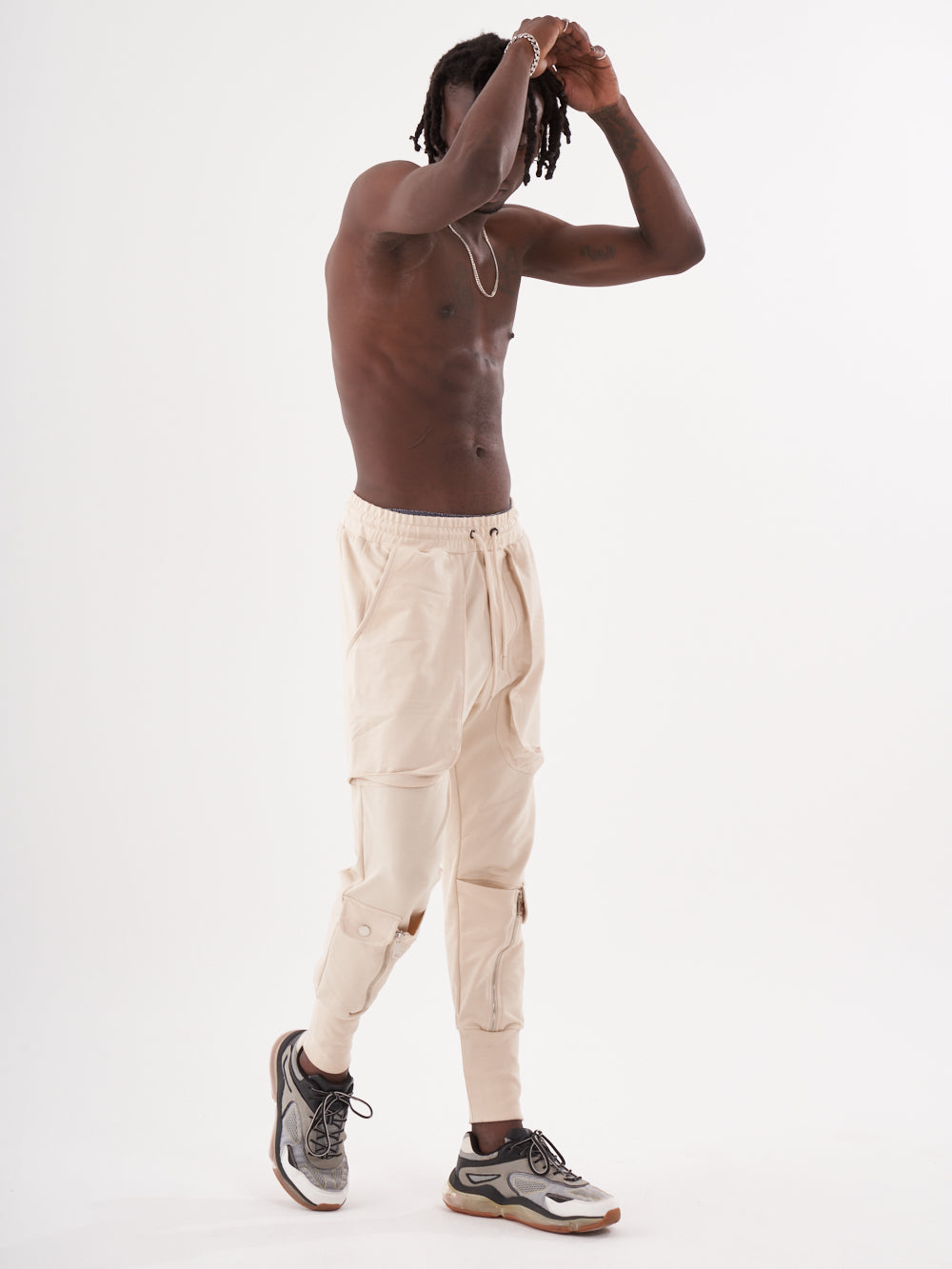 A man in GUERRILLA | BEIGE sweatpants is posing in front of a white background.