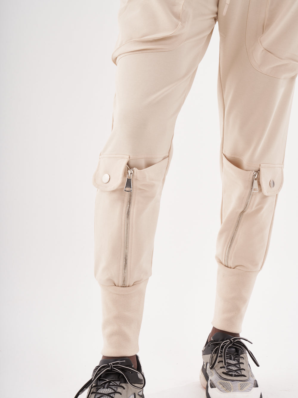 A man wearing a pair of stylish GUERRILLA | BEIGE jogging pants and comfortable sneakers.