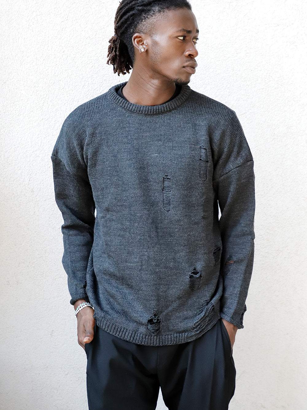 A man donning a DISTRESSED GENTLEMAN SWEATER | CHARCOAL and black pants with a soft feel.