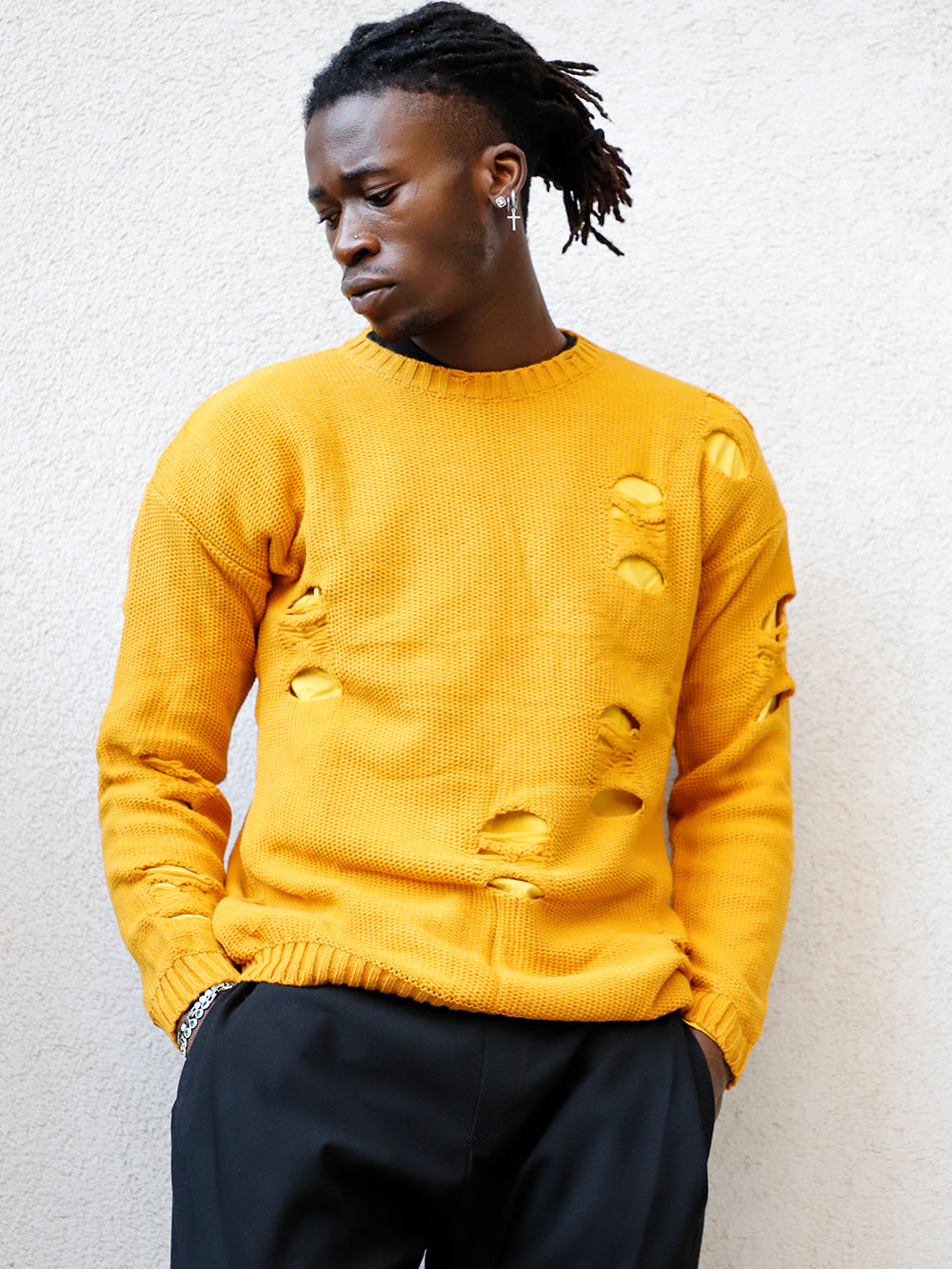 A man in a yellow sweater leaning against a wall, wearing a DISTRESSED DOUBLE LAYER SWEATER // MUSTARD.