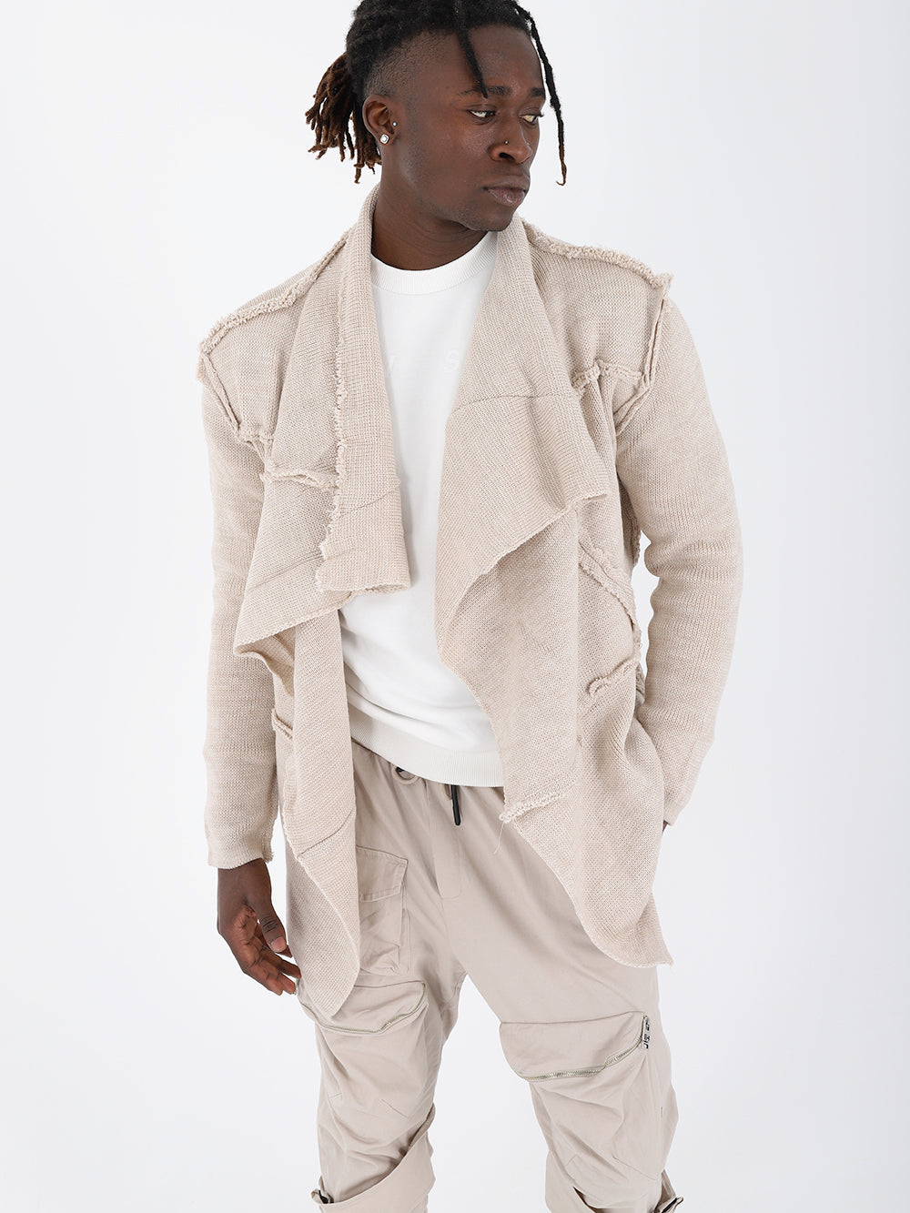 A man wearing an ASYMMETRIC SHORT CARDIGAN // IVORY in a beige jacket and tan pants, with a true to size fit.