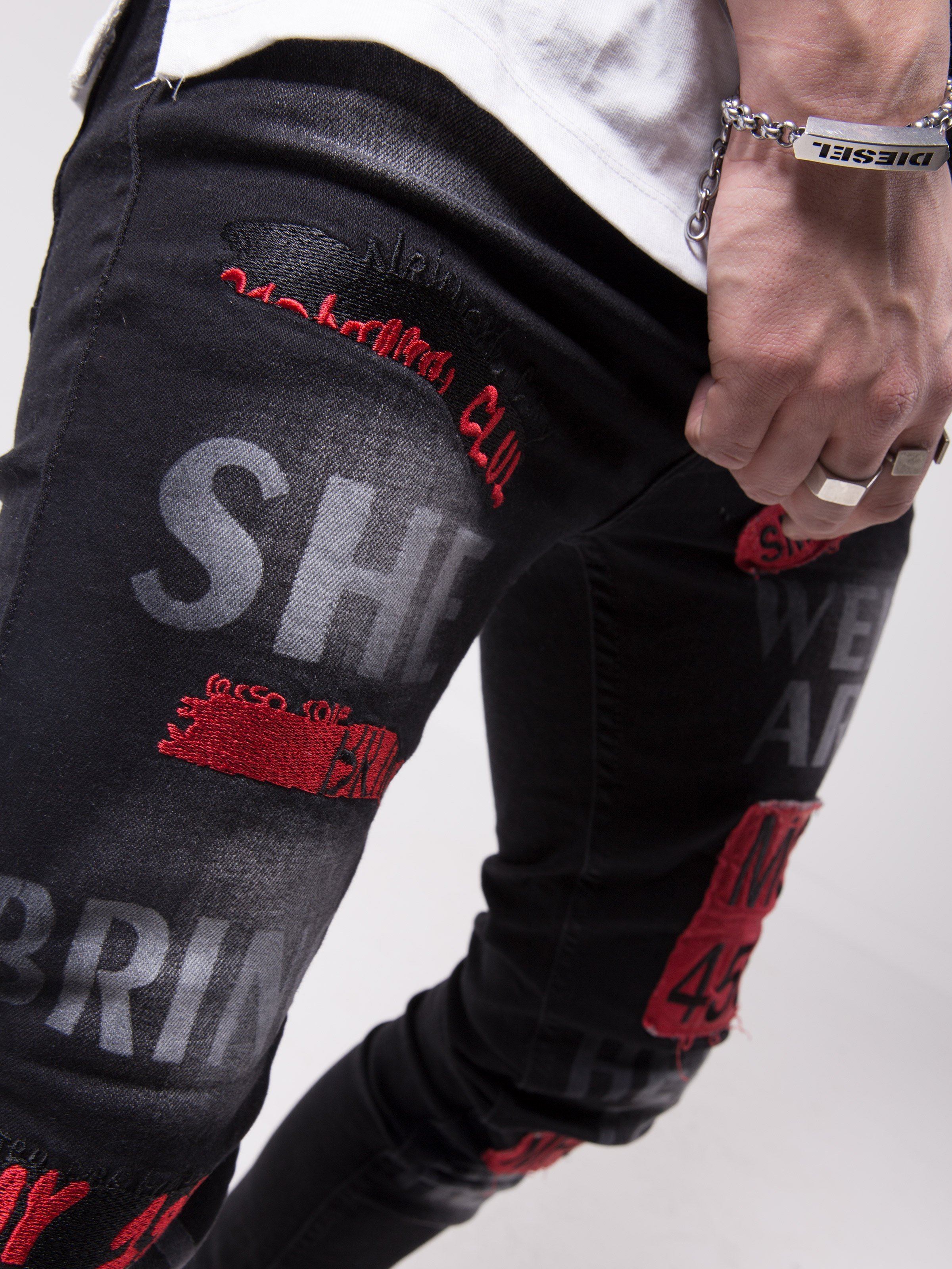 A man wearing a pair of GHETTO BIRD jeans with red writing on them.