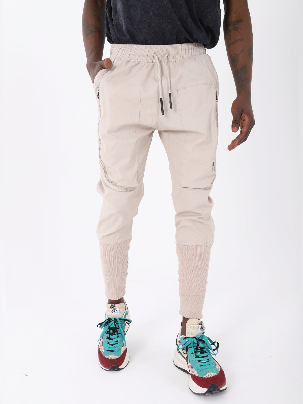 A man donning fashionable ankle sock joggers paired with sneakers and a beige ALTIS JOGGERS with an adjustable drawstring waist.