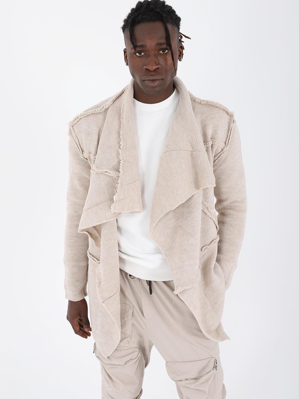 A black man wearing a beige jacket and white pants with the ASYMMETRIC SHORT CARDIGAN // IVORY.