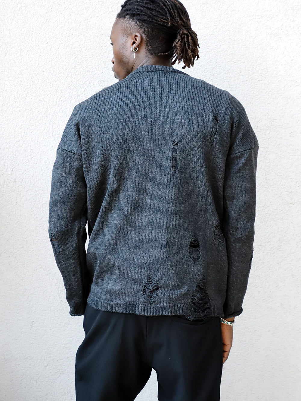 A man with dreadlocks wearing a DISTRESSED GENTLEMAN SWEATER | CHARCOAL and black pants.