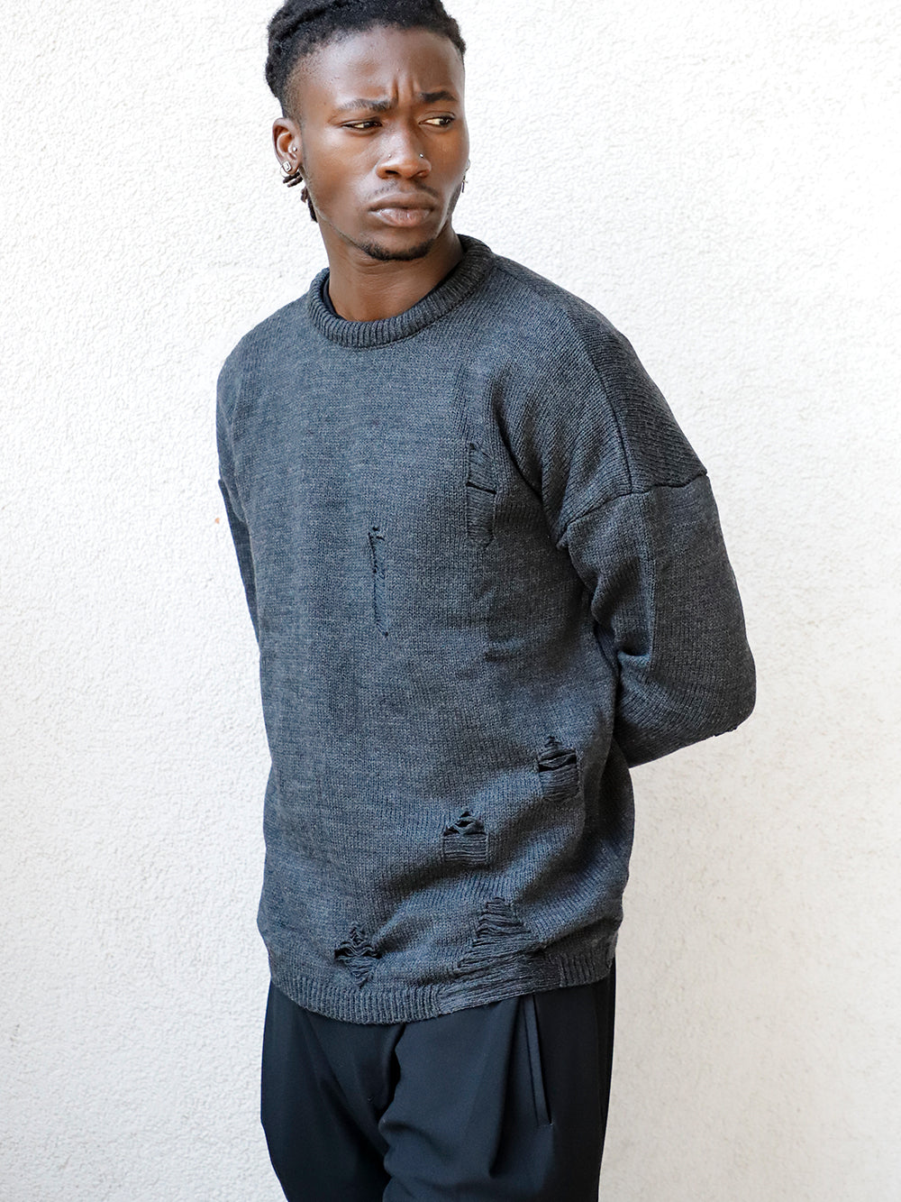 A man wearing a DISTRESSED GENTLEMAN SWEATER | CHARCOAL and black pants.