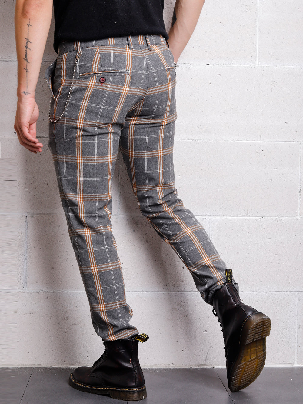 A man is leaning against a wall wearing CHECKERED STONE pants.