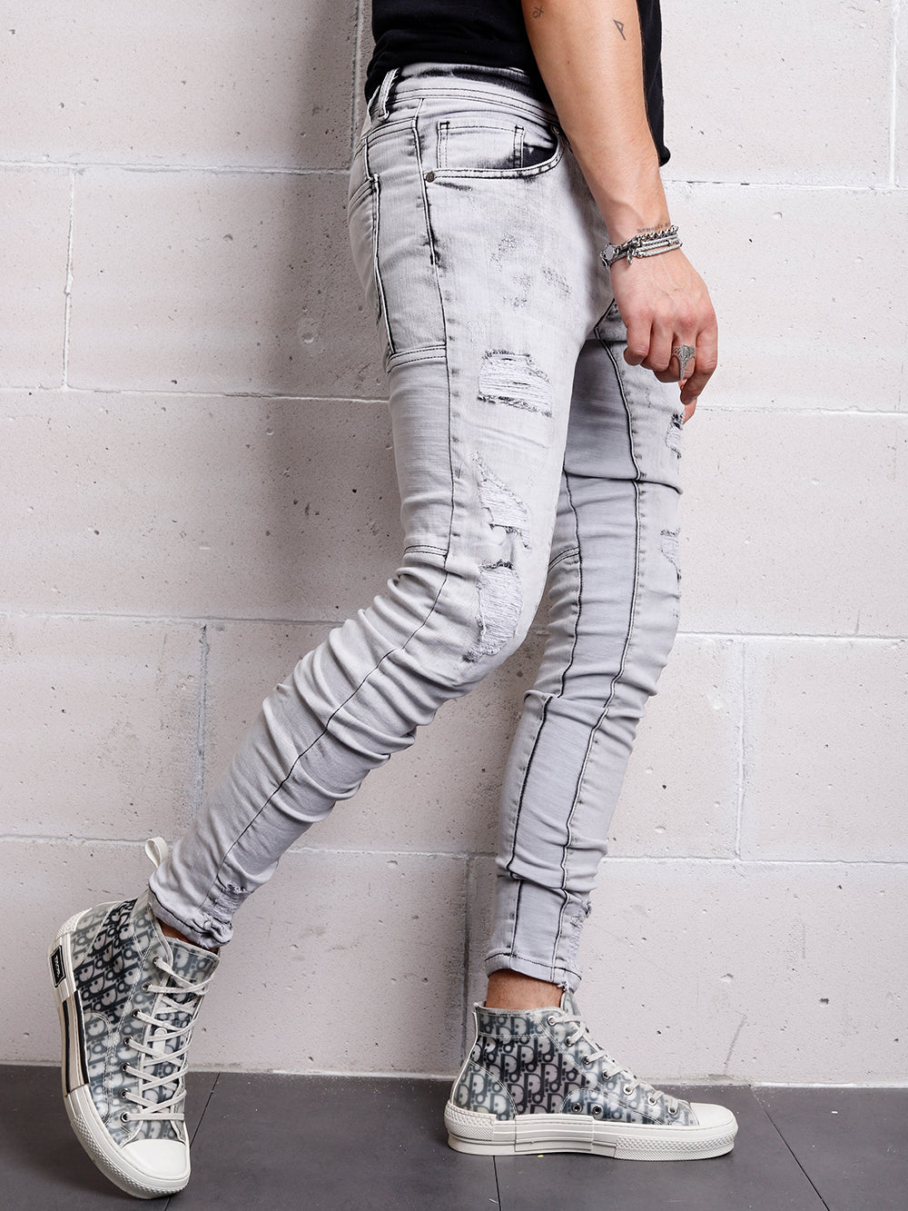 A man wearing distressed jeans and CLOUD 9 sneakers leaning against a wall.