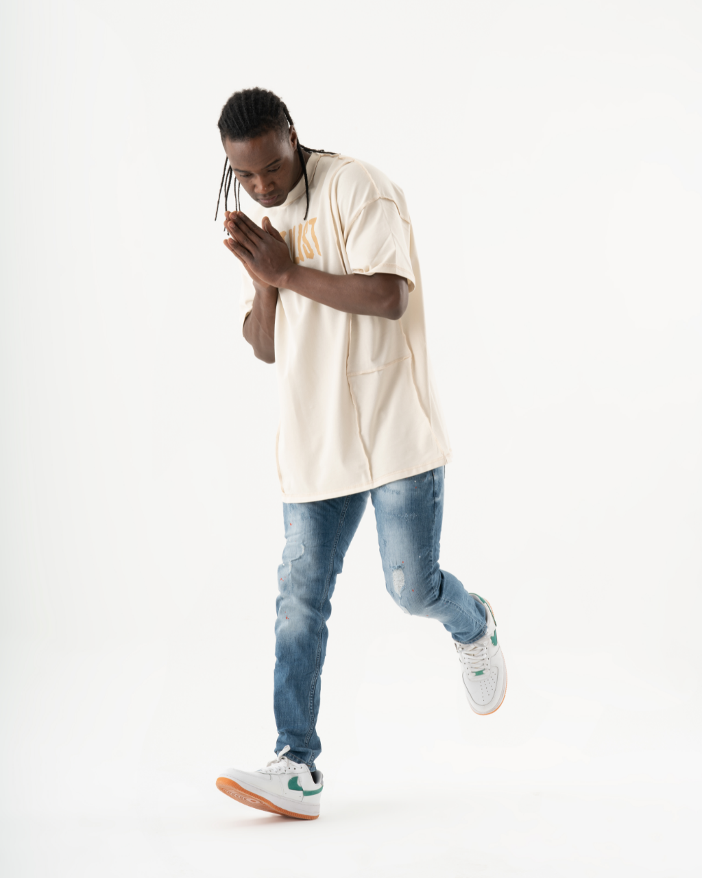 A man in a TEZAR t-shirt and ripped jeans standing on a white background.