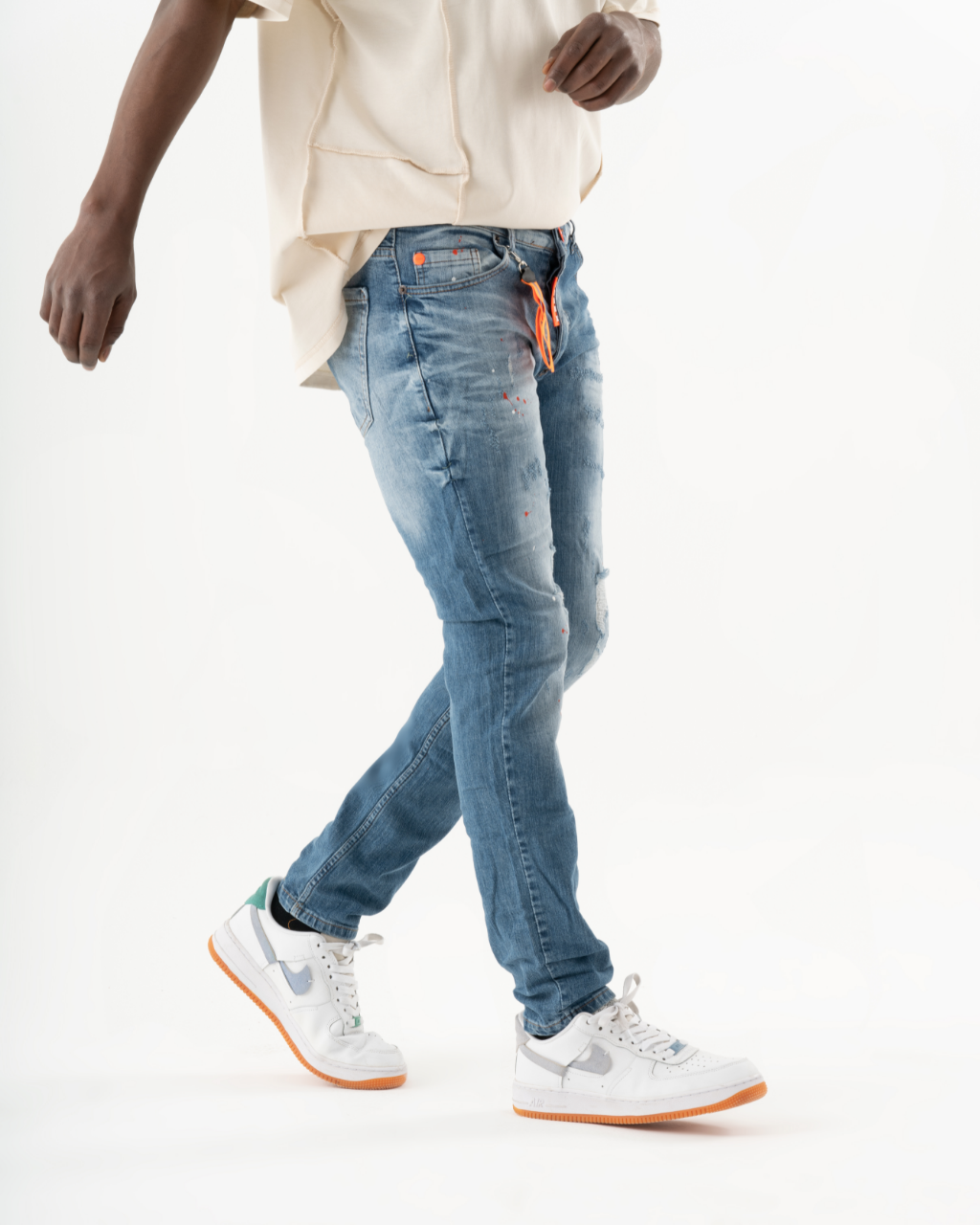 A man in blue jeans and orange TEZAR sneakers is walking.