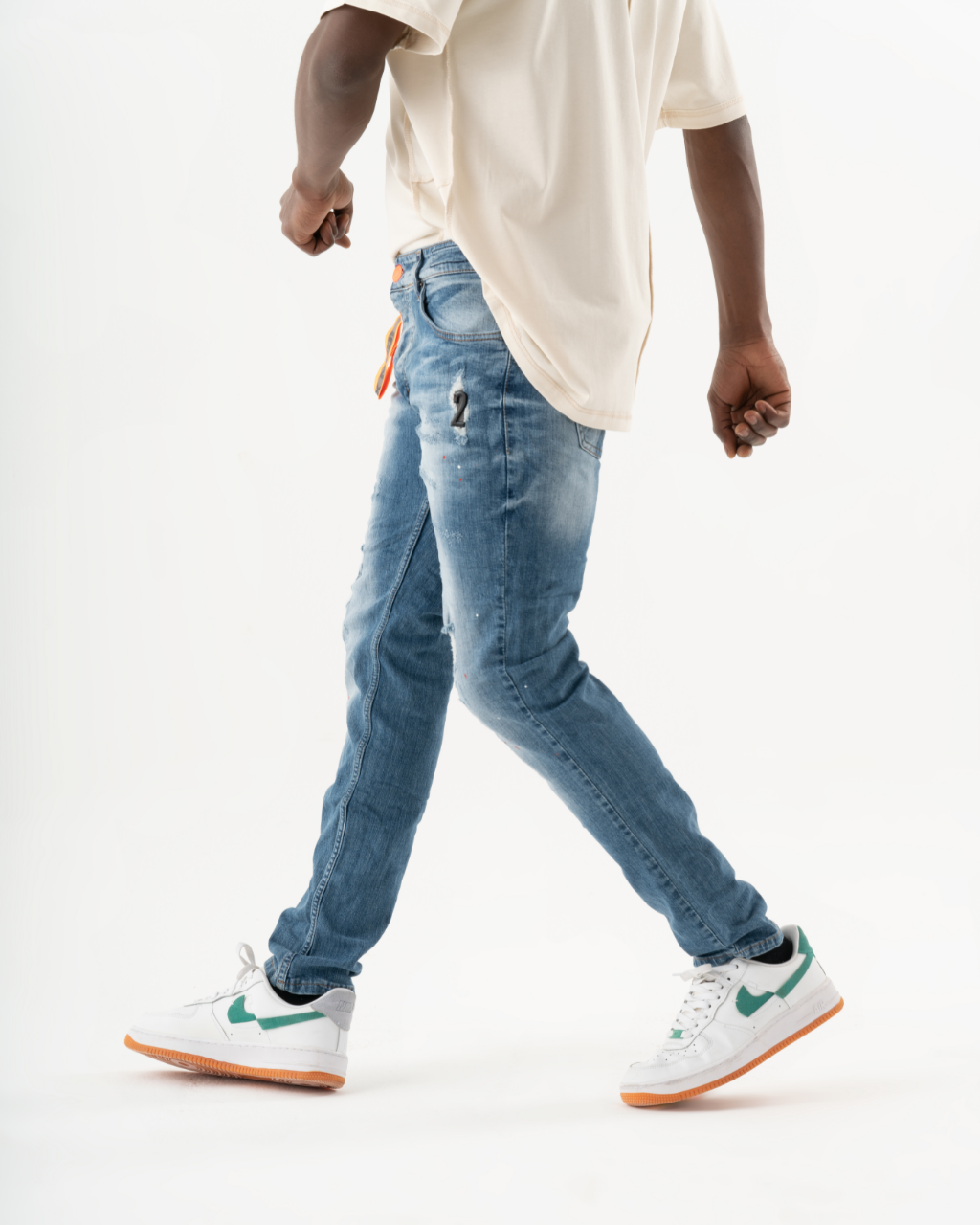 A man in ripped jeans and sneakers walking on a TEZAR background.