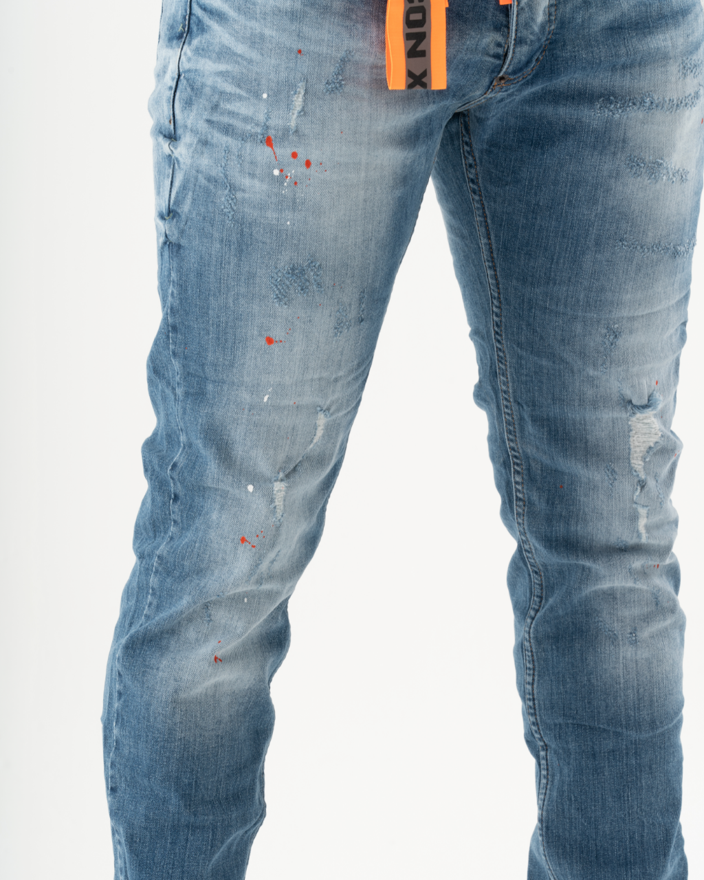 A man wearing a pair of TEZAR skinny fit jeans with orange paint splatters and patches.