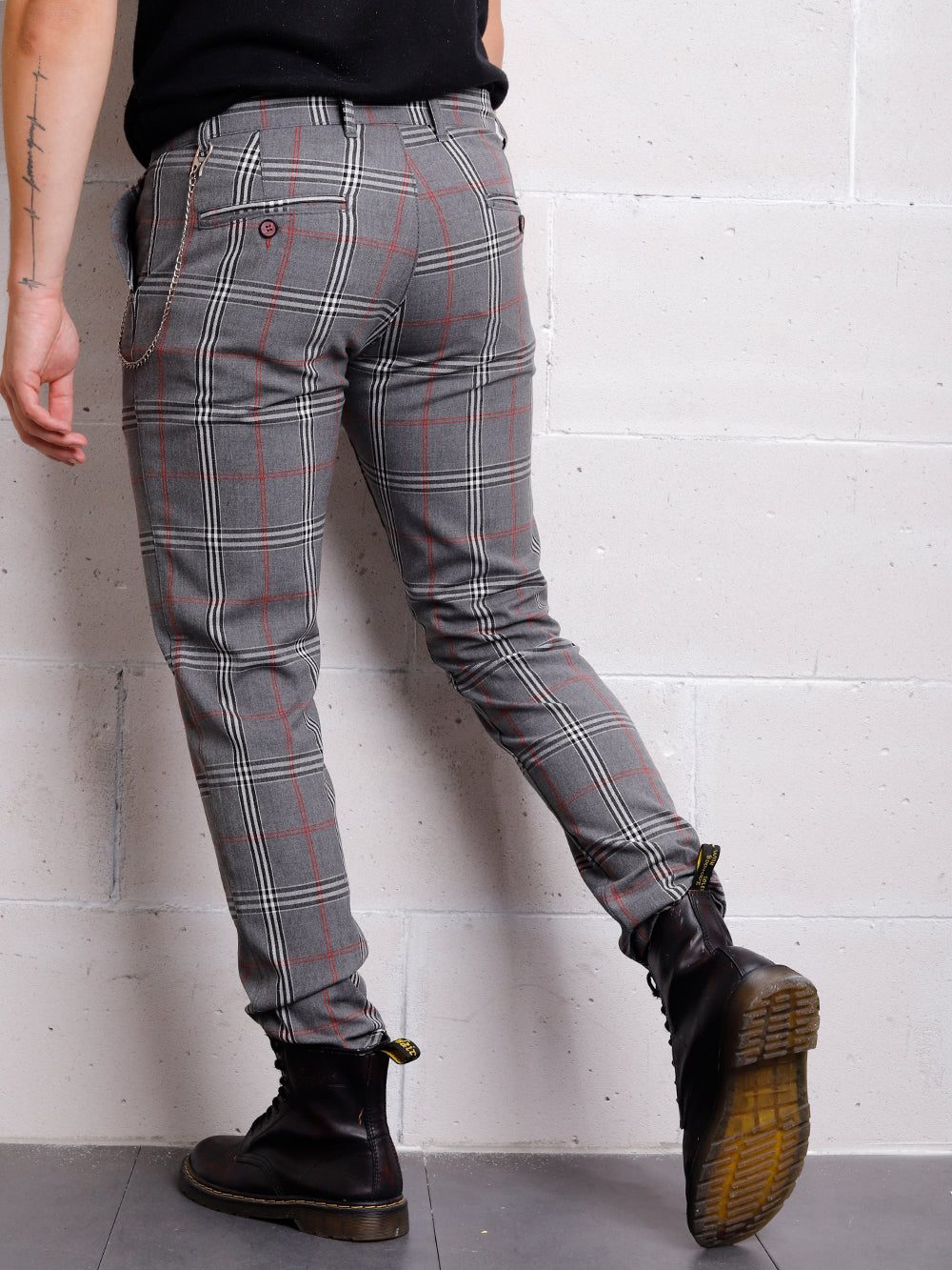 A man is standing against a wall wearing CHECKERED GREY pants.