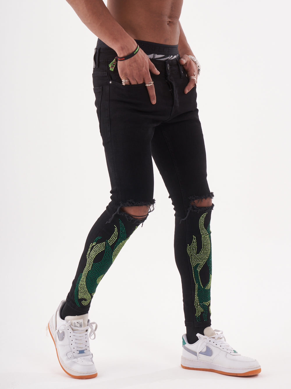 A man wearing HELLFIRE | GREEN ripped rhinestone jeans and white sneakers.