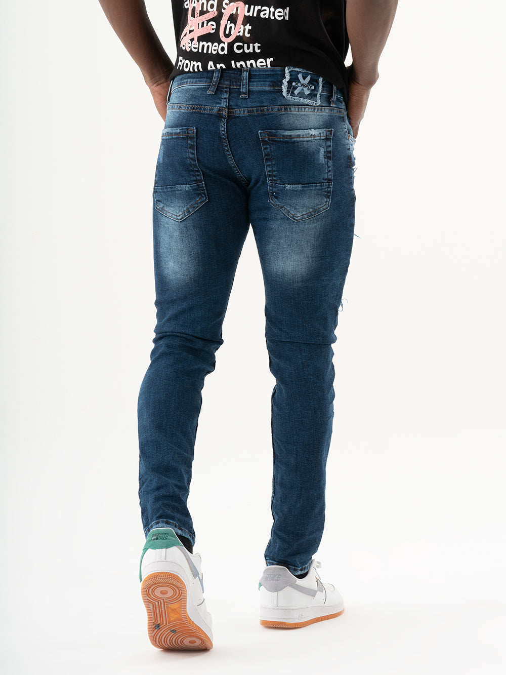 A man wearing skinny fit jeans and a INJUN | BLUE t-shirt from a mens streetwear brand.