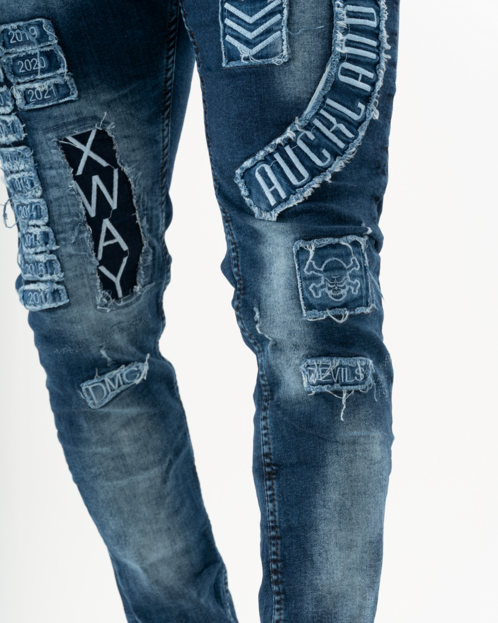 A man wearing a pair of INJUN | BLUE jeans with patches on them.