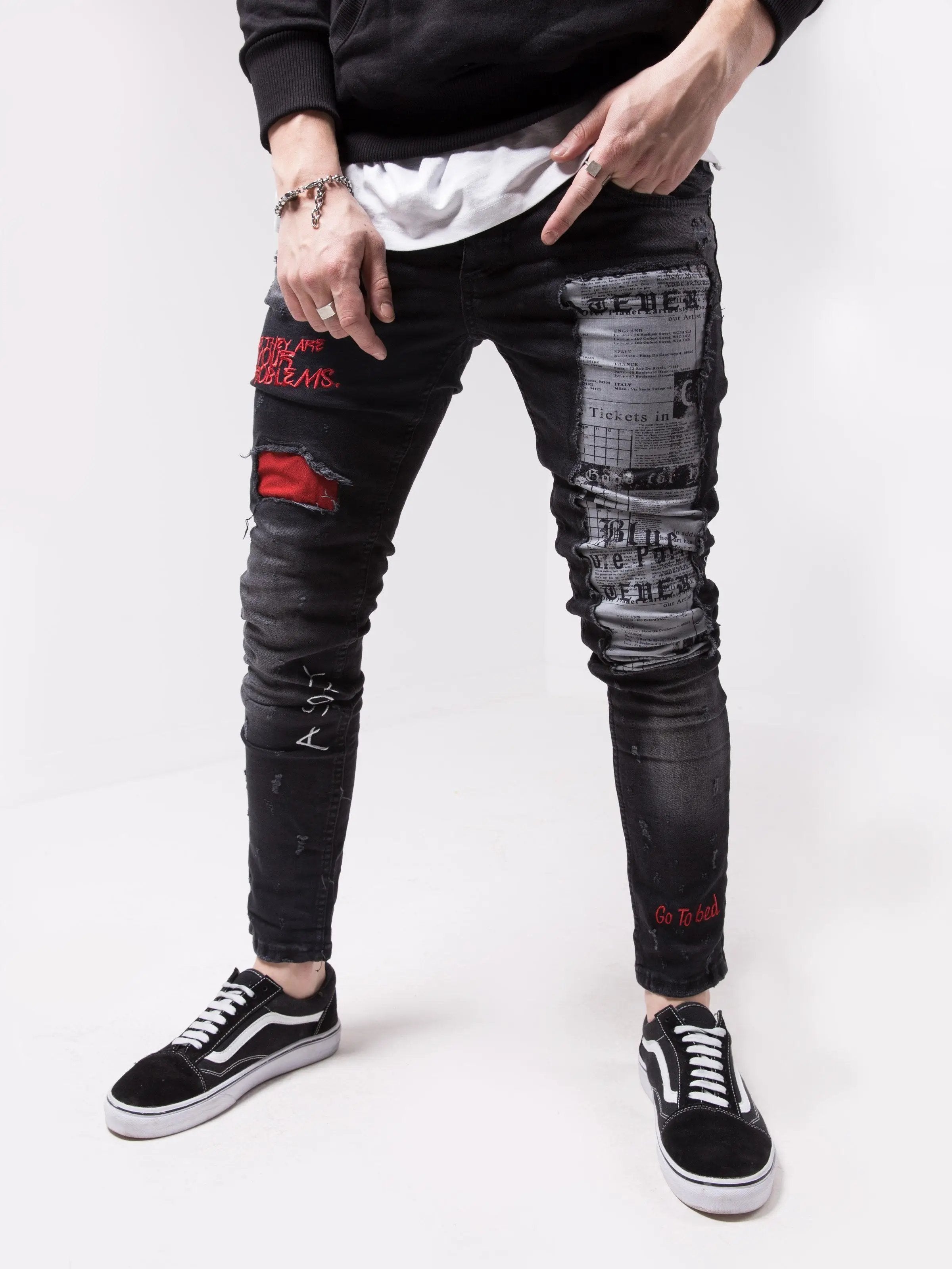 A man wearing a pair of black SKYSCRAPER jeans with red patches.