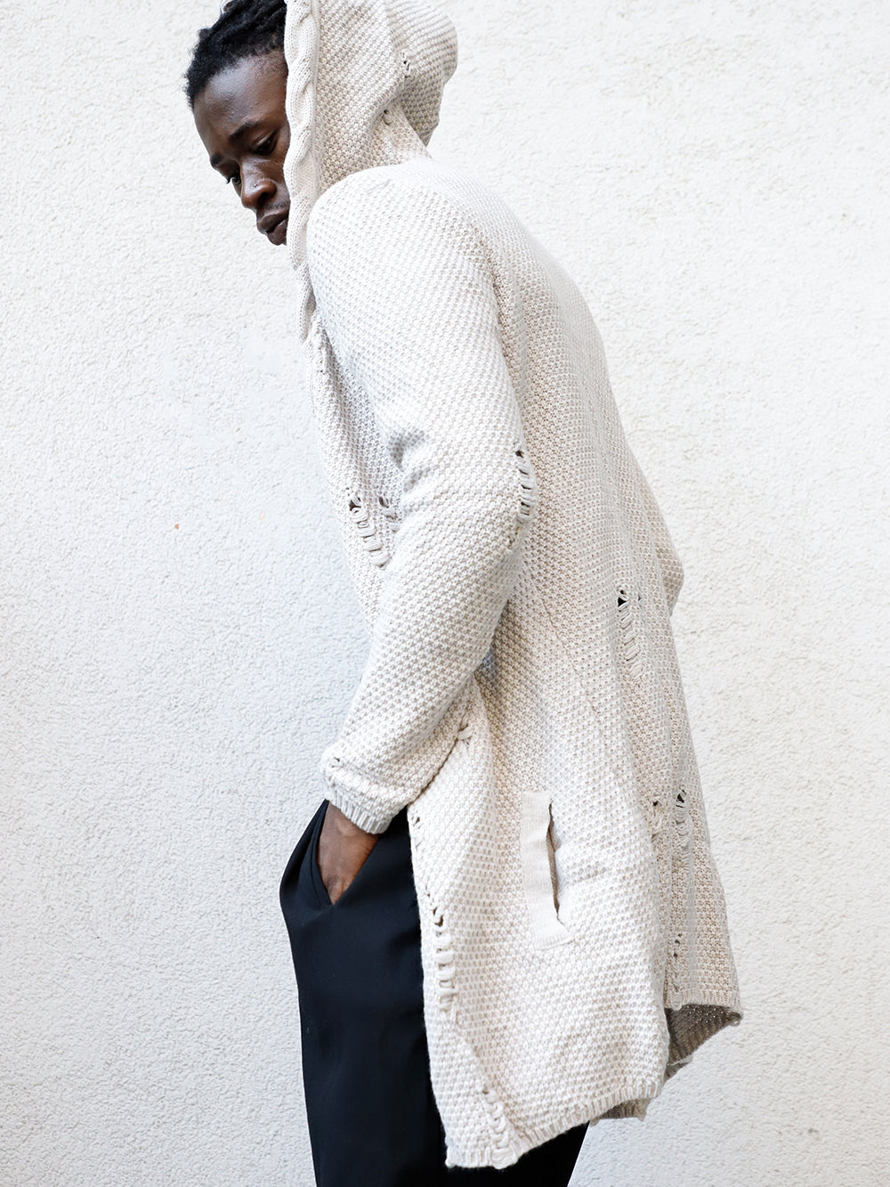 A man in a HOODED DISTRESSED CARDIGAN // STONE standing next to a wall, wearing skinny fit jeans.