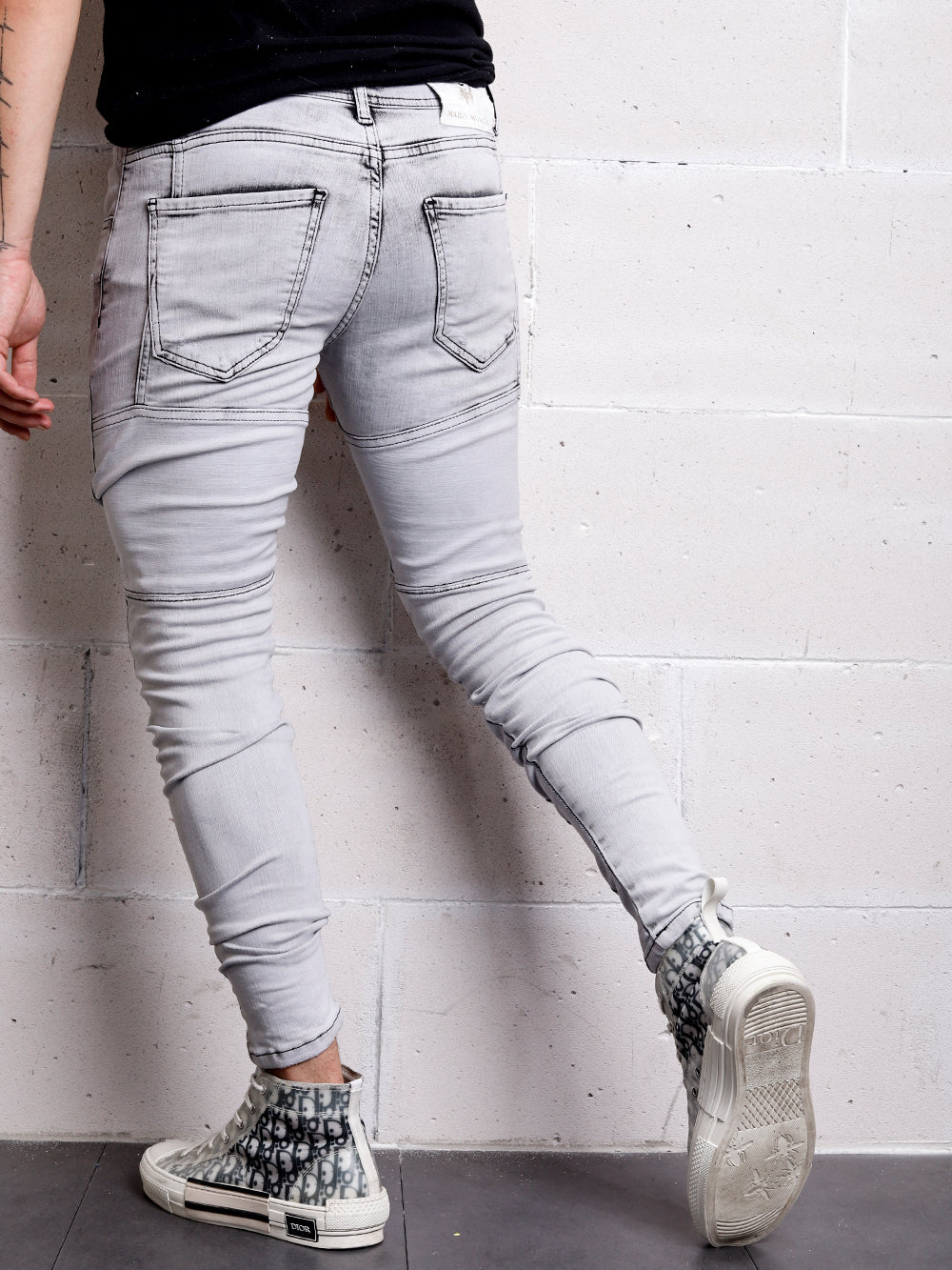 A man in CLOUD 9 distressed denim jeans leaning against a wall.