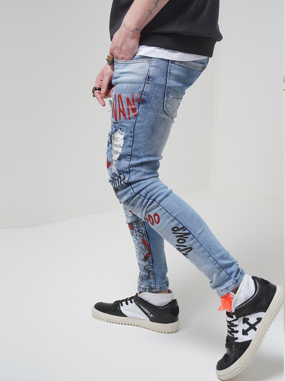 A man wearing BANKSY ripped jeans and sneakers.