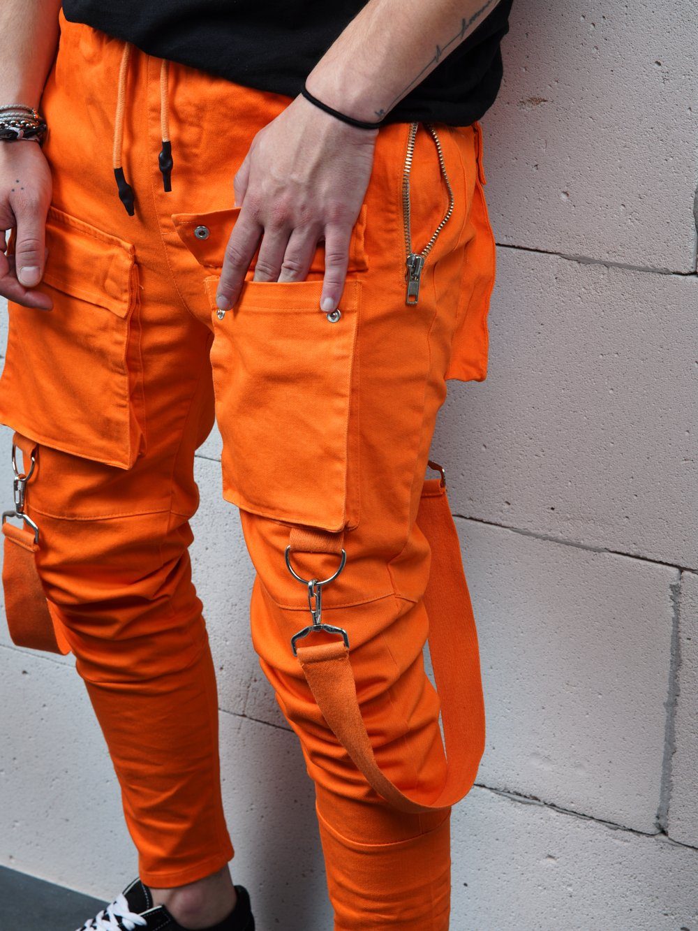 A man in ORANGE BRONX cargo pants is standing against a wall.