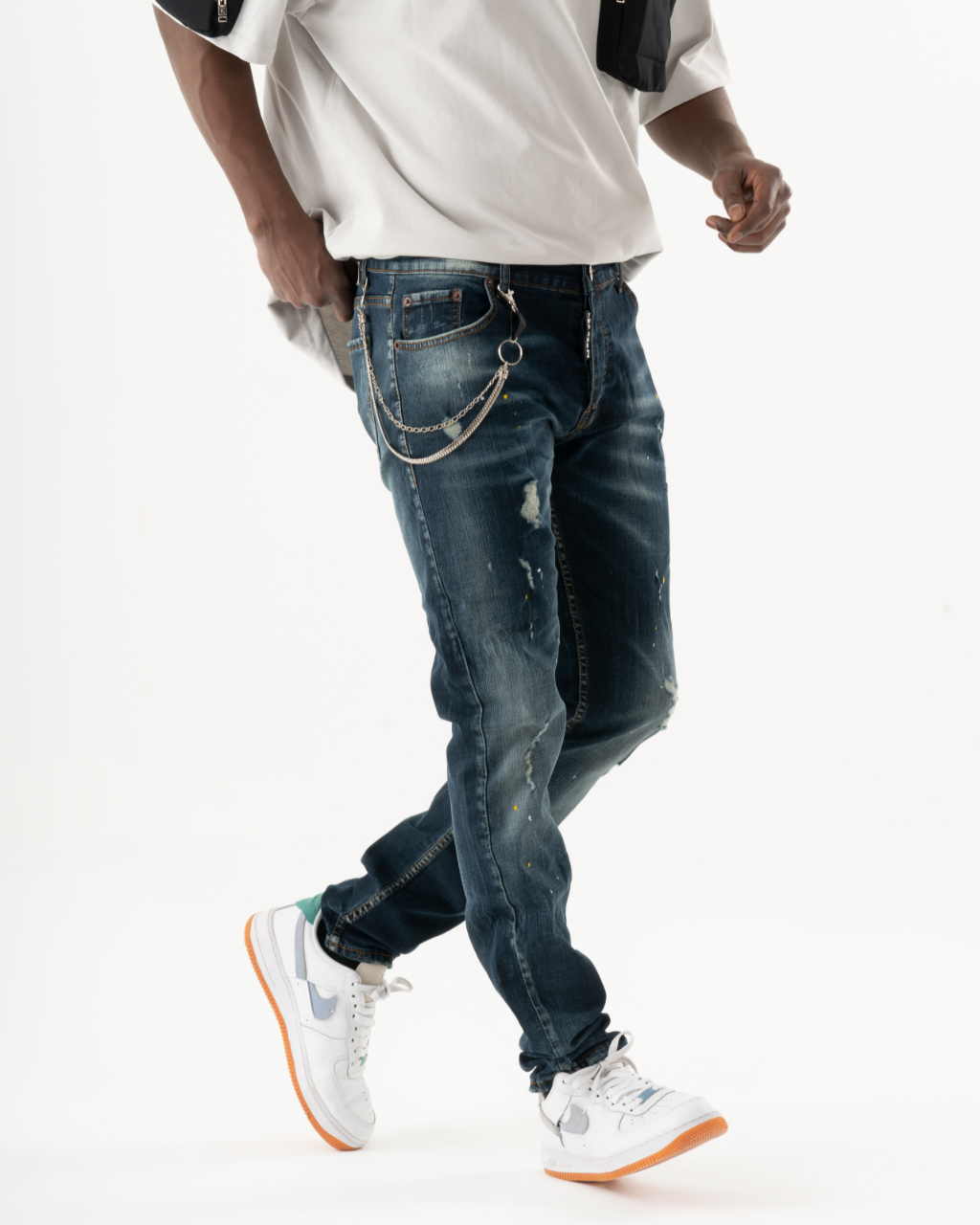 A man in KUDOS blue jeans and white sneakers is walking in front of a white background.