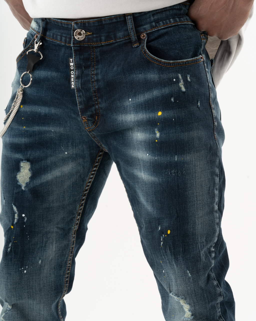 A man is wearing a pair of KUDOS jeans with stains on them.