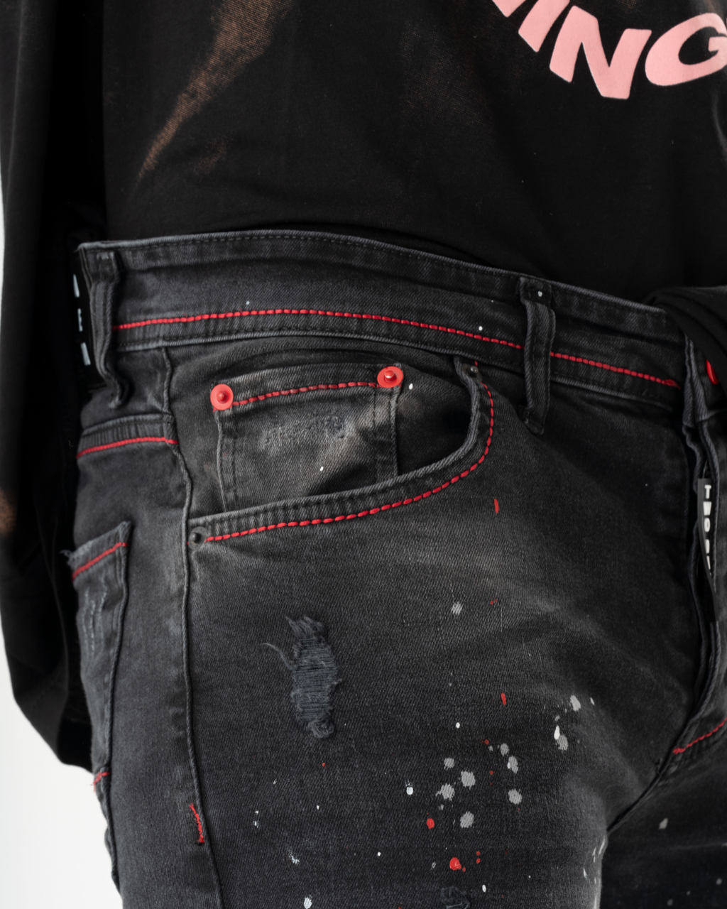 The back of a man's ripped black jeans with red paint splatters.