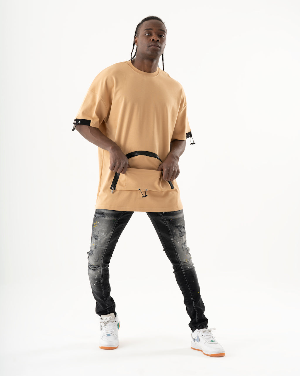 A man wearing a tan ENRAGE t-shirt and jeans, made of elastic fabric for a smooth feel.