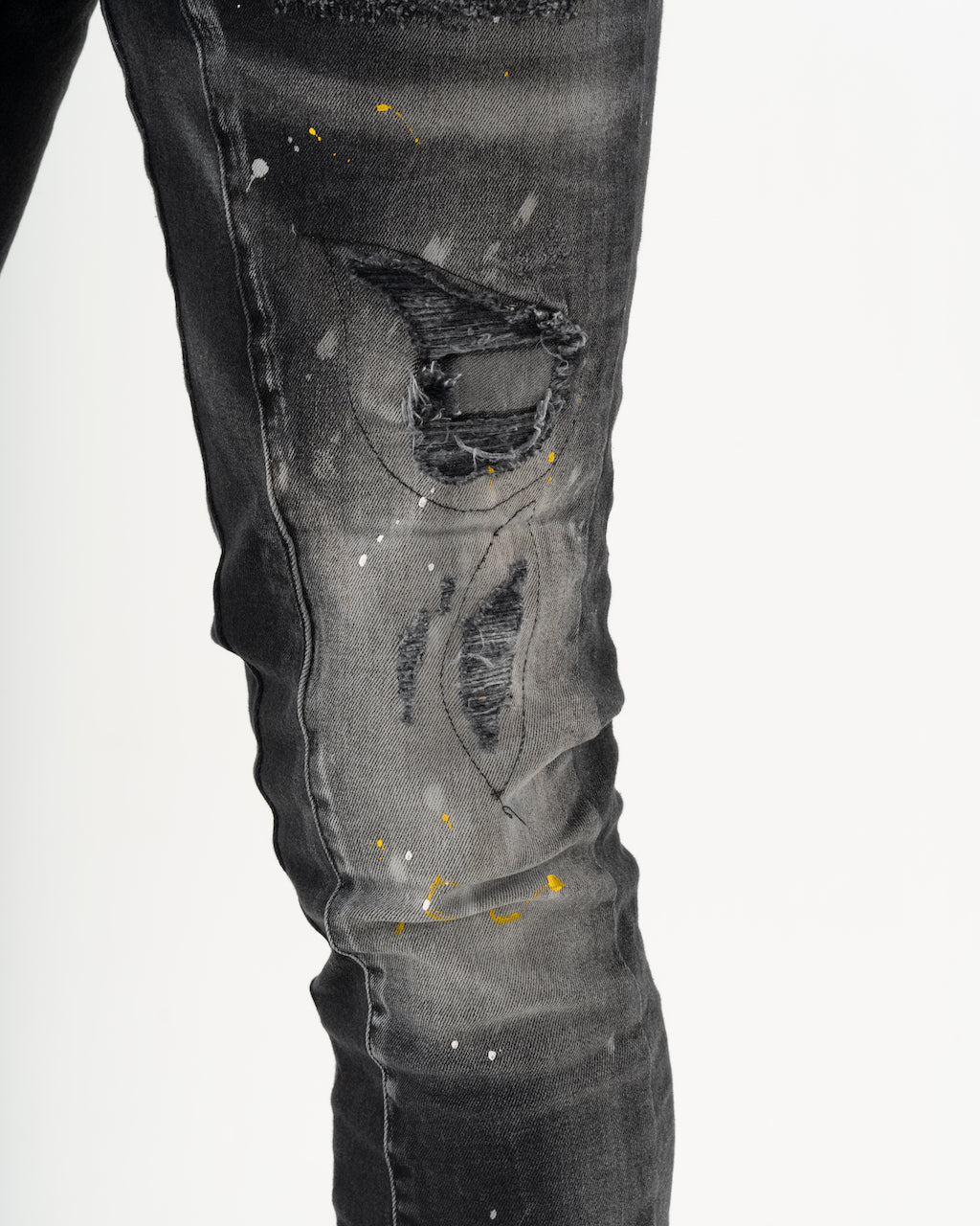 A pair of ENRAGE skinny fit black jeans with yellow paint splattered on them.
