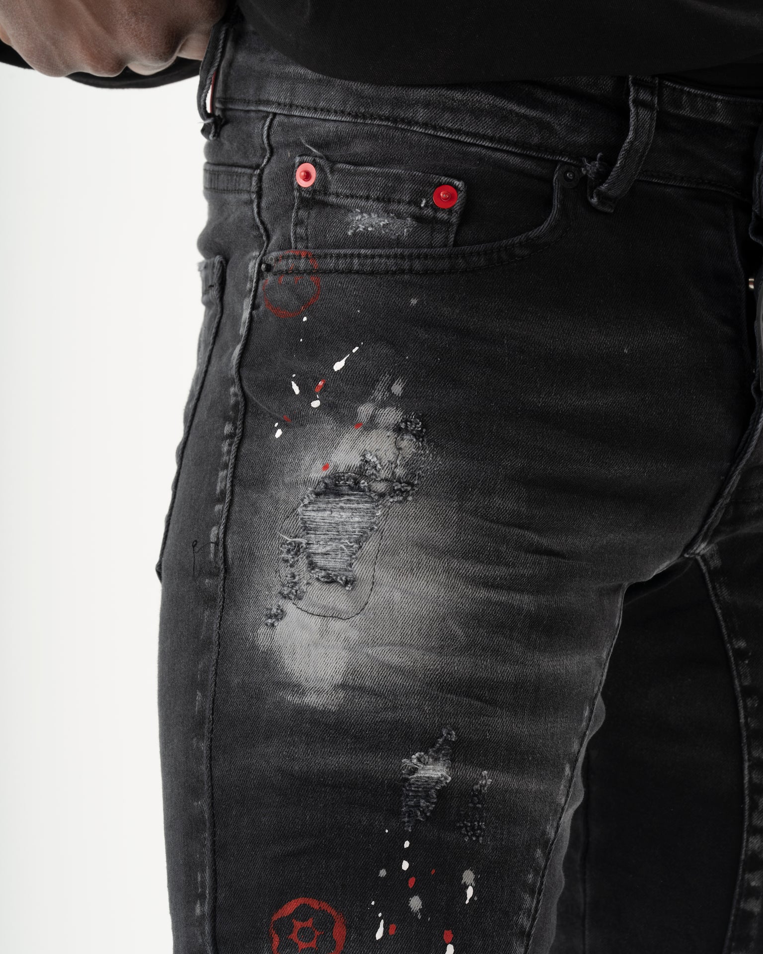 A man is wearing a pair of black skinny-fit THUNDERBIRD jeans with added stretch and red paint on them.