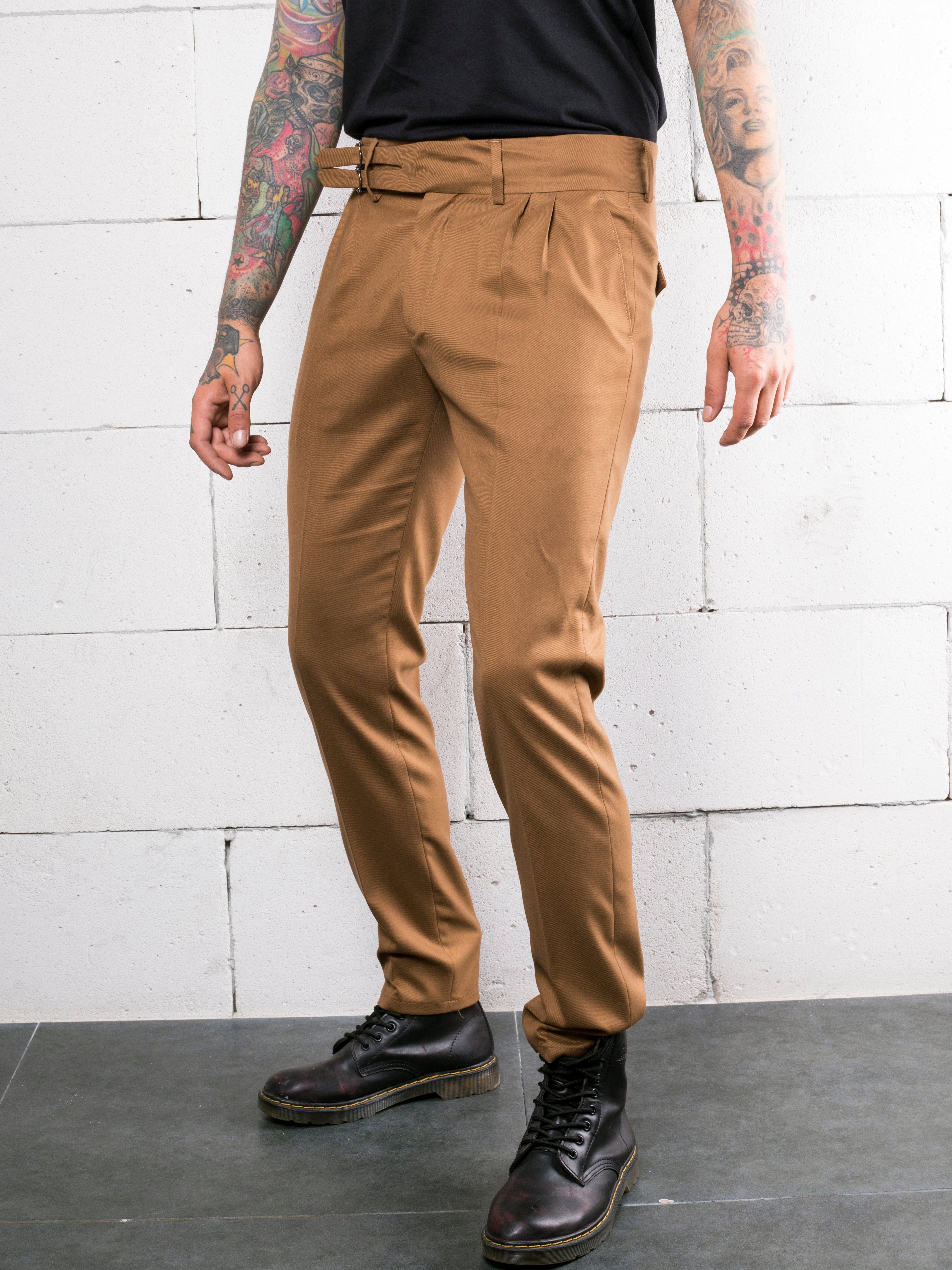 A man with tattoos wearing tan chino pants made of CROISSANT fabric.