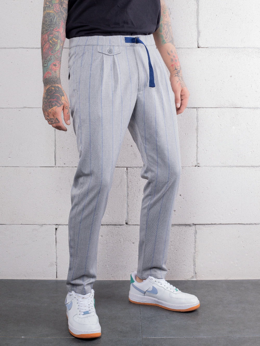 A man with tattoos is standing in front of a brick wall wearing RODEO DRIVE PANTS made from premium Italian fabric.