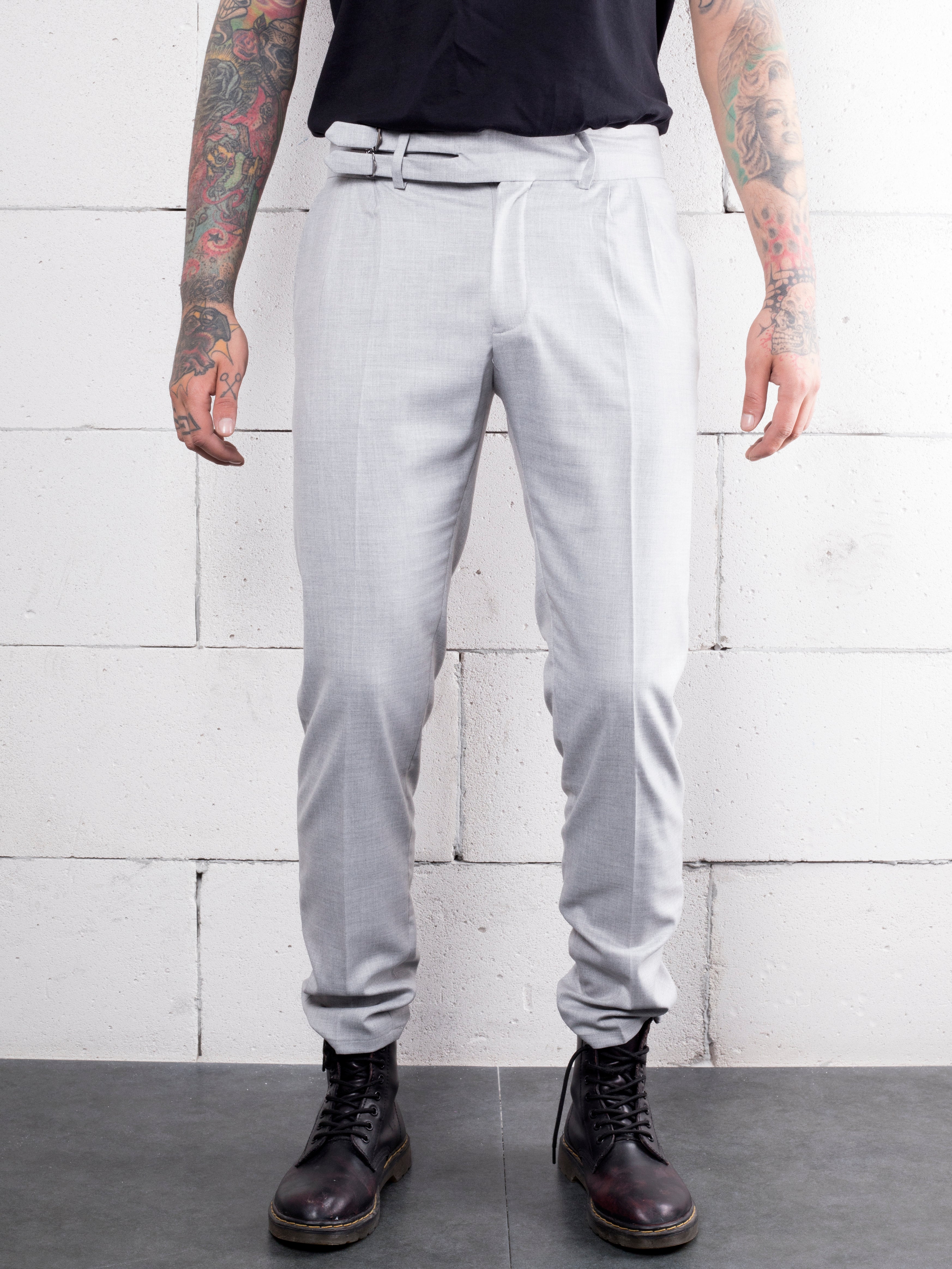 A man with tattoos is standing in front of a white wall wearing GRANITE PANTS made from premium Italian fabric.