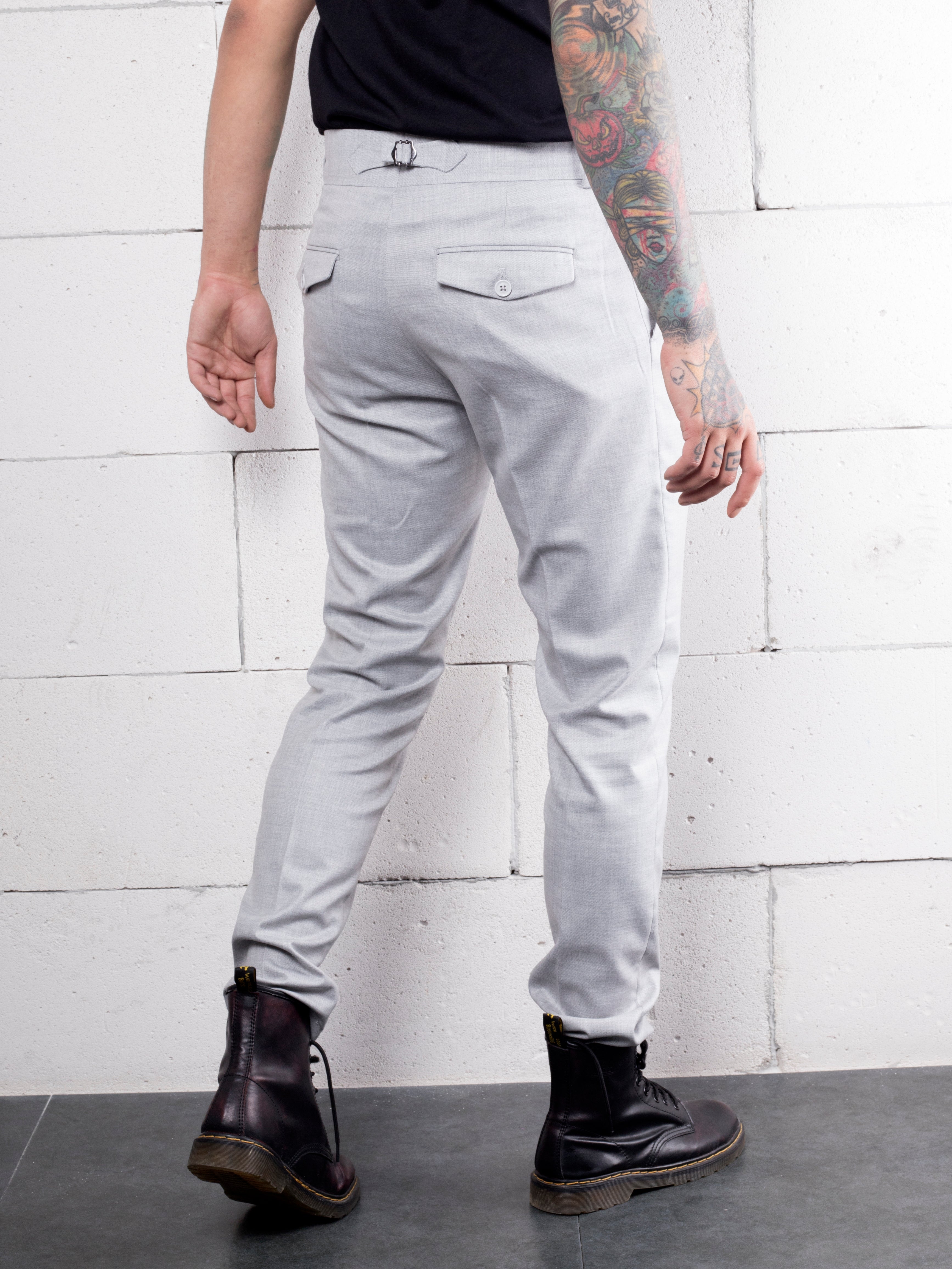 A man with tattoos wearing slim-fit grey Granite pants made from premium Italian fabric.