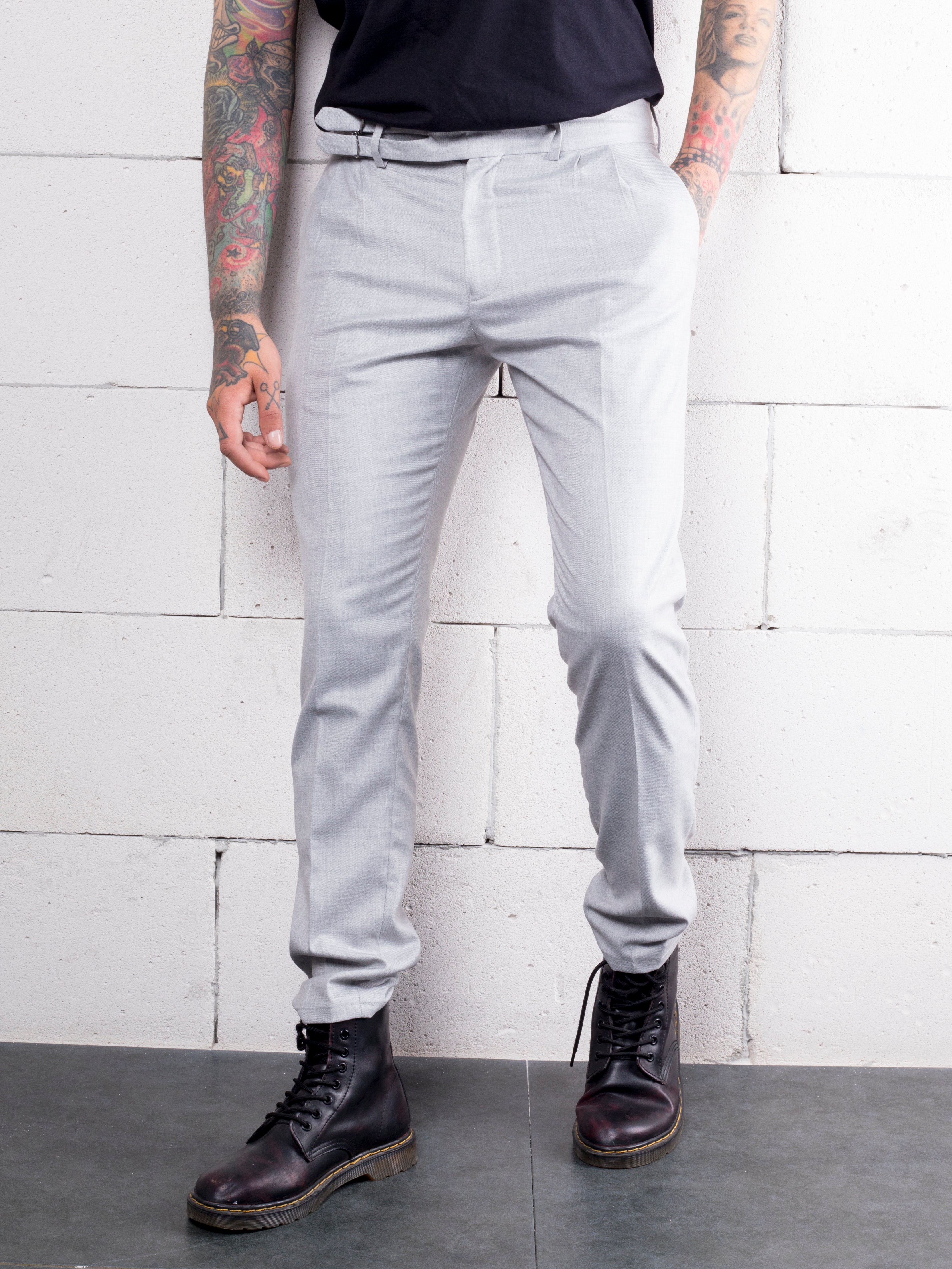A man with tattoos is standing next to a wall, wearing Granite Pants made from Premium Italian fabric.
