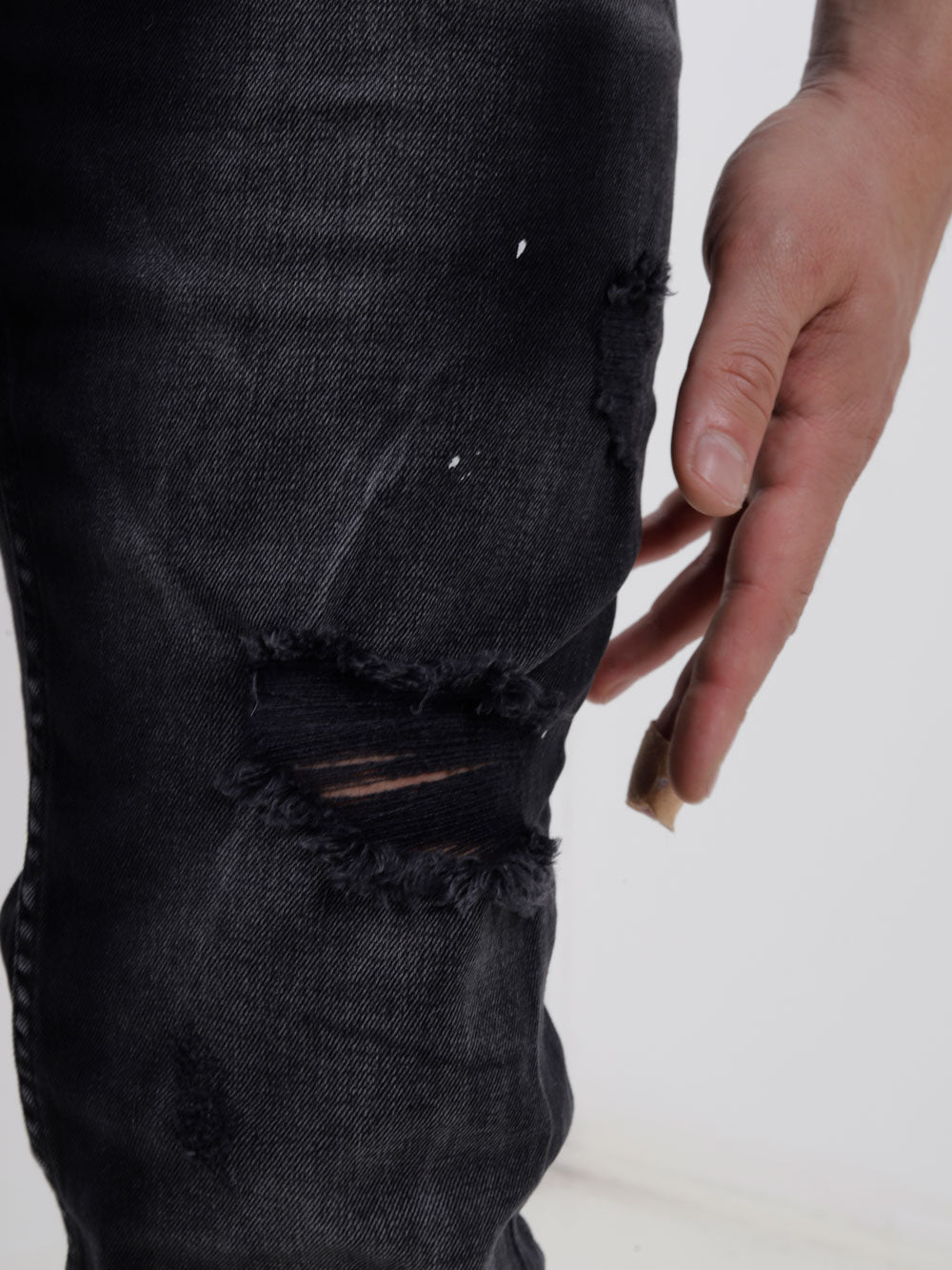 A man is holding a pair of MODERO black jeans with holes in them.