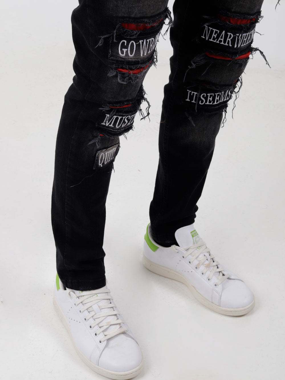 A man wearing PAW TRAIL ripped jeans and sneakers.