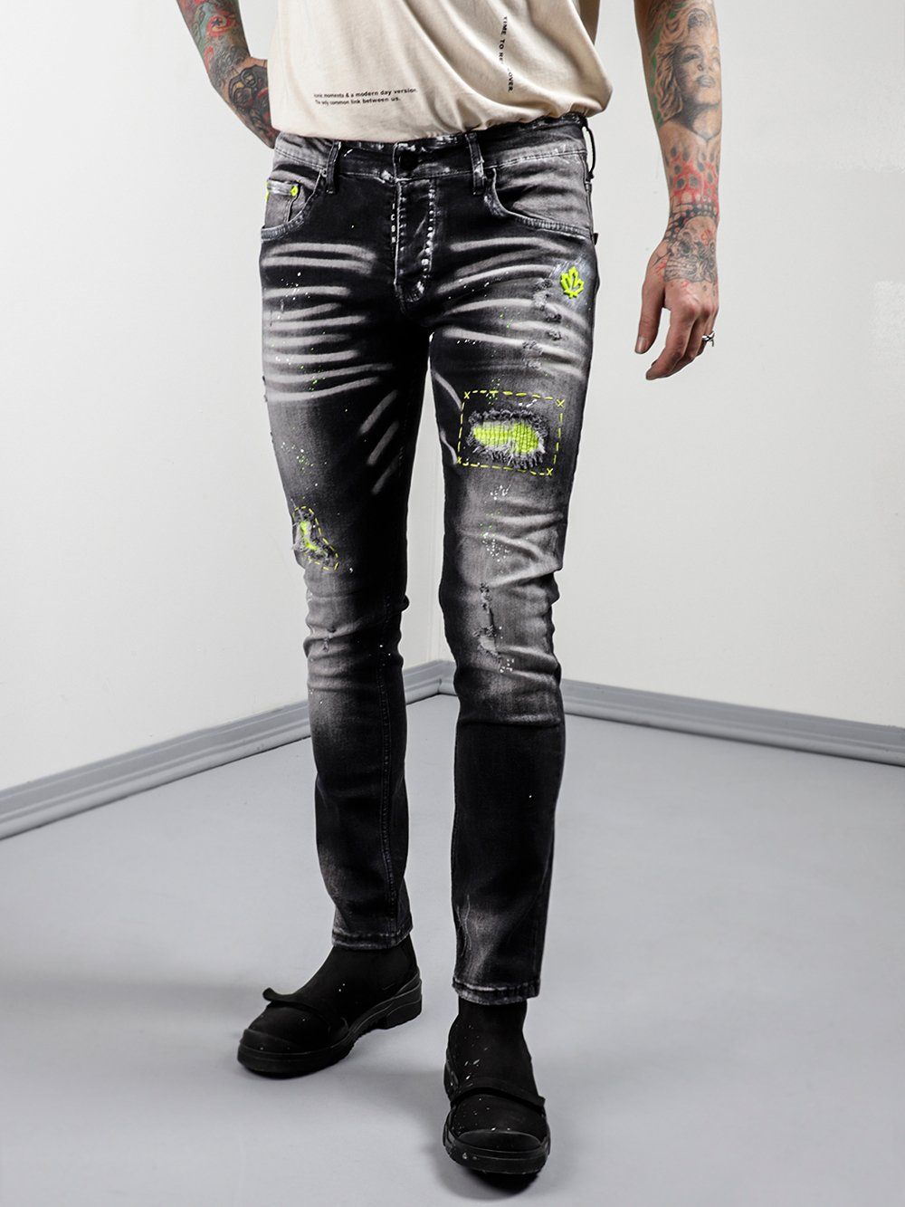 A man in NEON TALK jeans with tattoos standing in front of a white wall.