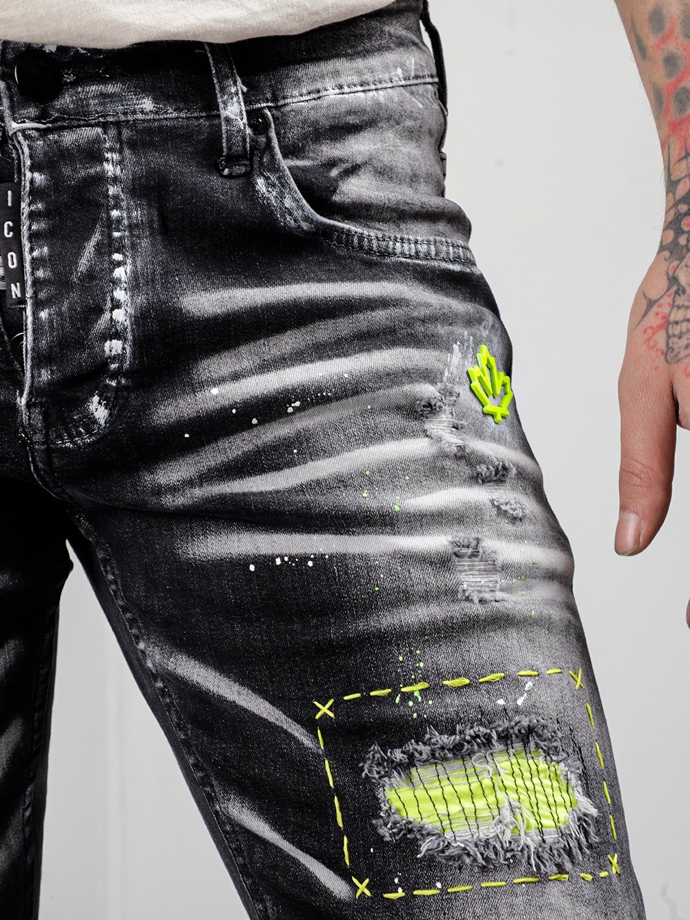 A man is wearing a pair of NEON TALK jeans with yellow paint on them.