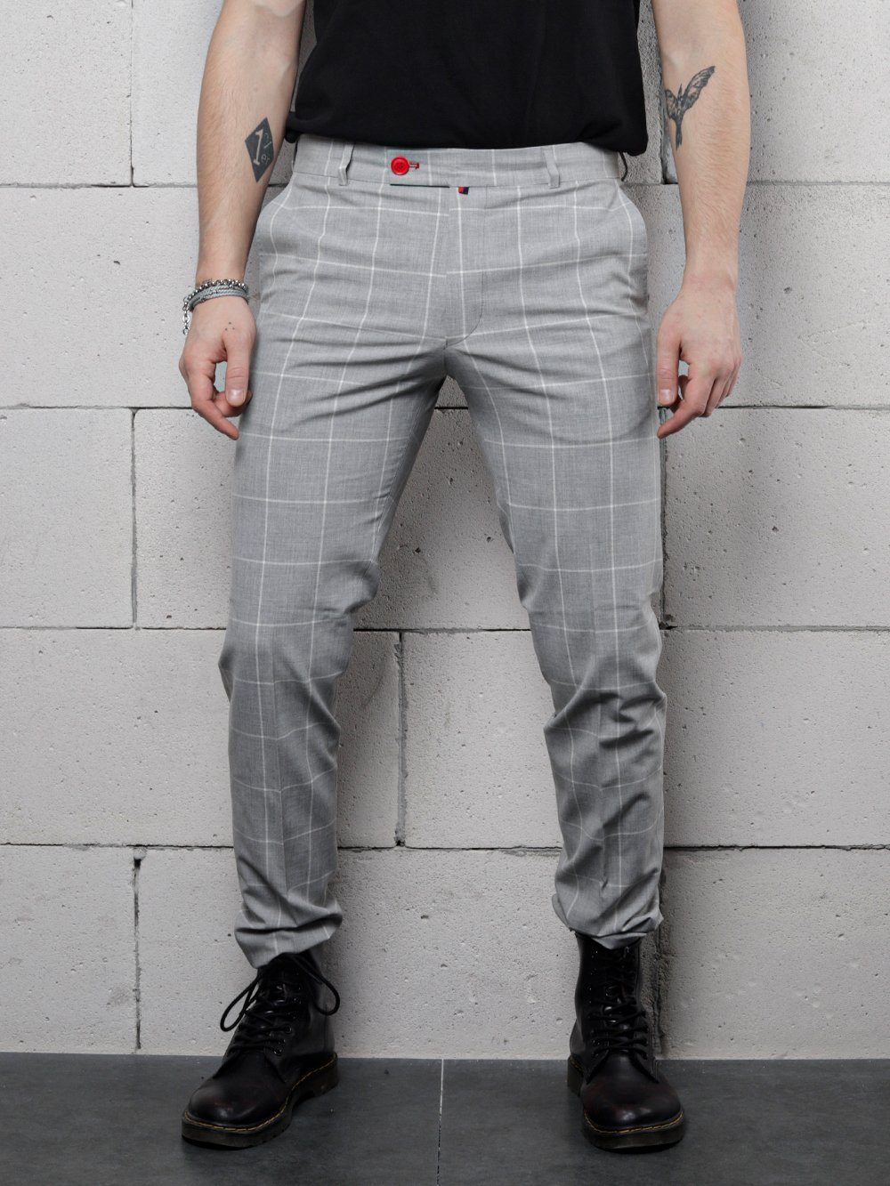 A man is standing against a brick wall wearing ICED AMERICANO PANTS.