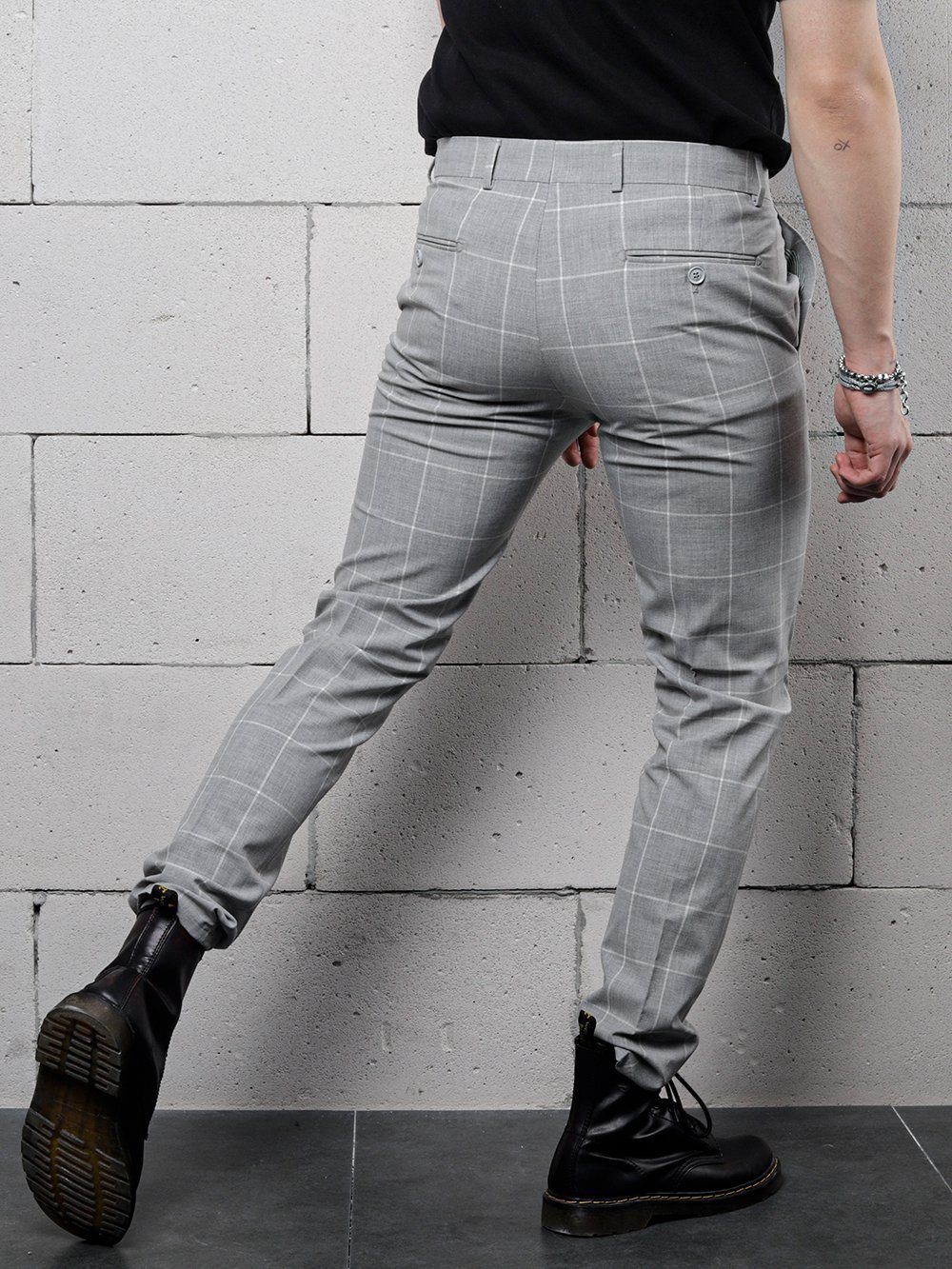 A man wearing ICED AMERICANO PANTS is standing with his back to a wall.